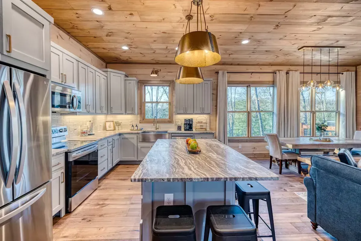 Modern kitchen with stainless steel appliances, large island, wood ceiling, and windows overlooking trees