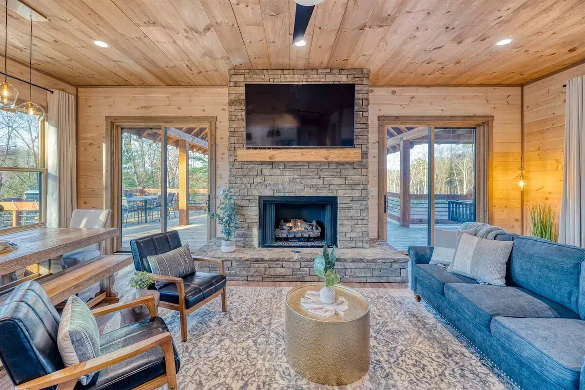 Cozy cabin living room with stone fireplace, wall TV, large windows, and blue sofa