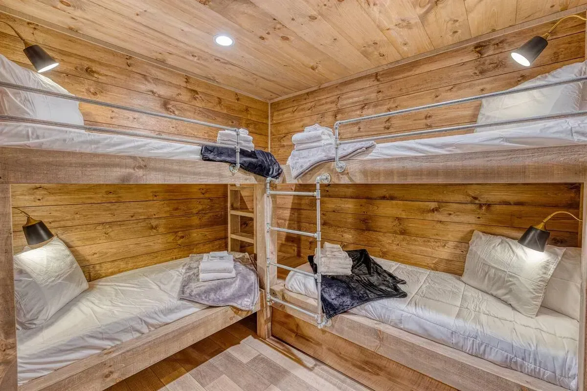 Wood-paneled bunk bedroom with four beds, white bedding, and a wooden ladder in the center