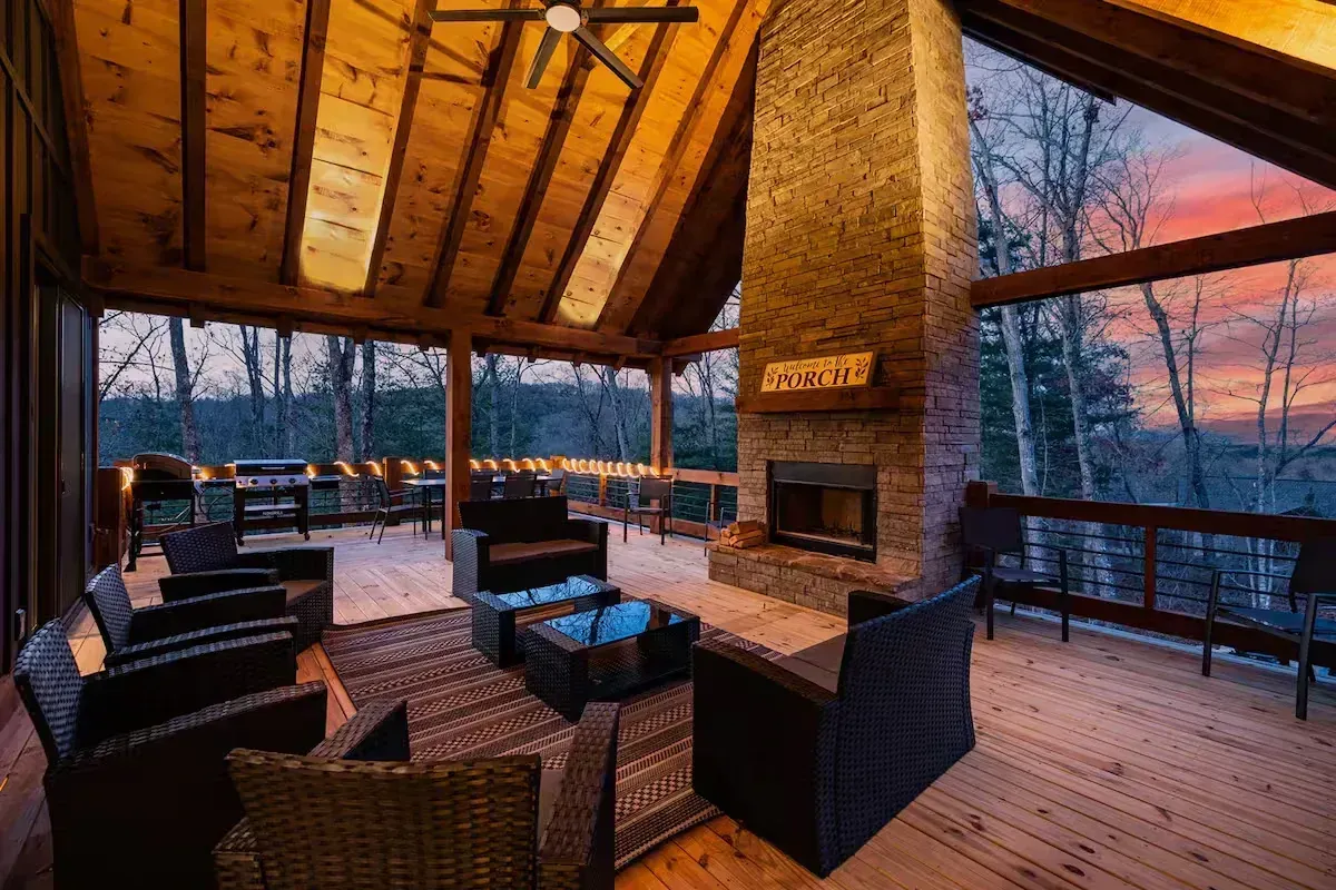 Cozy covered deck with wicker seating, stone fireplace, and warm sunset view through open railings