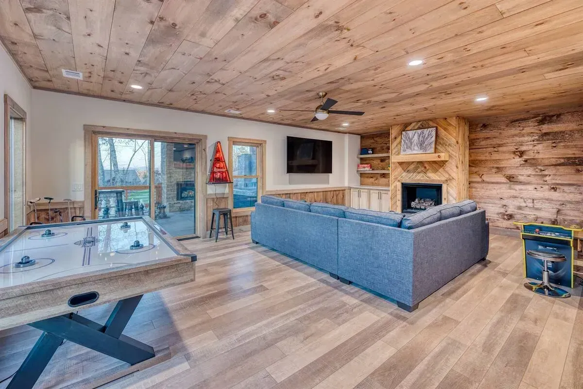 Cozy rustic living room with blue sectional, stone fireplace, wall TV, and foosball table