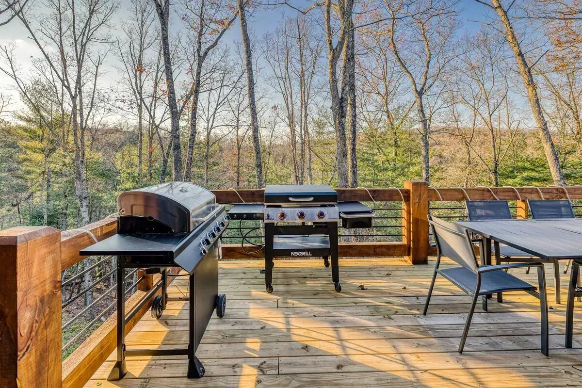 Outdoor deck with a grill, dining table, and wooded view in the background