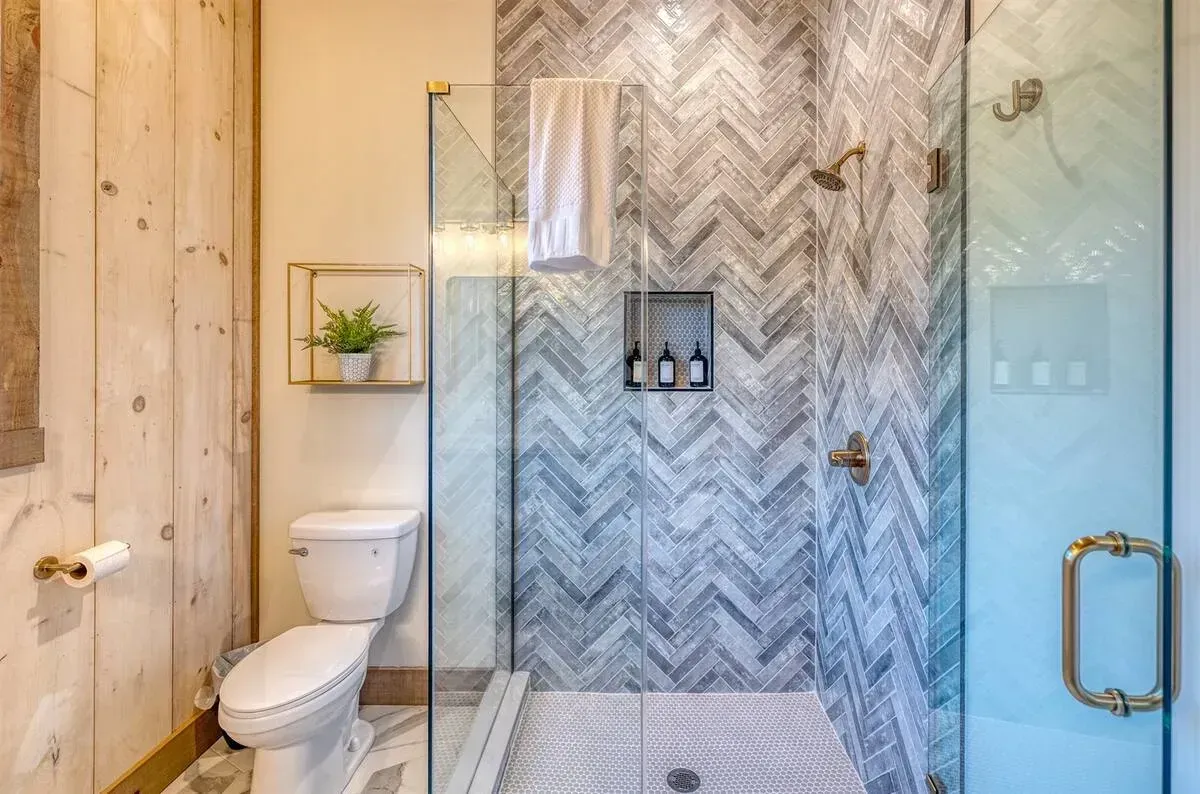 Modern bathroom with glass shower, white toilet, beige tile, and gold fixtures