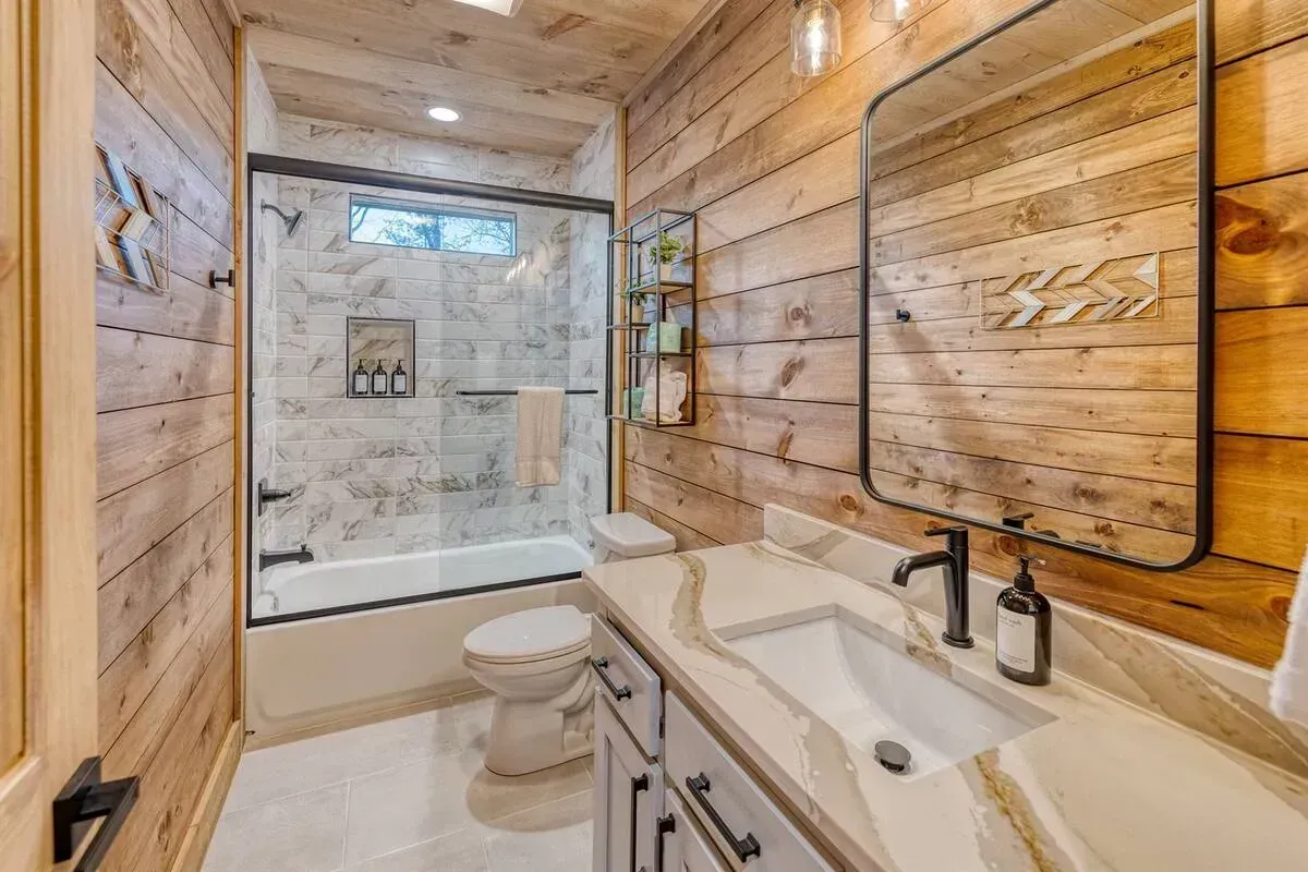 Bright rustic bathroom with wood walls, white vanity, toilet, and glass shower