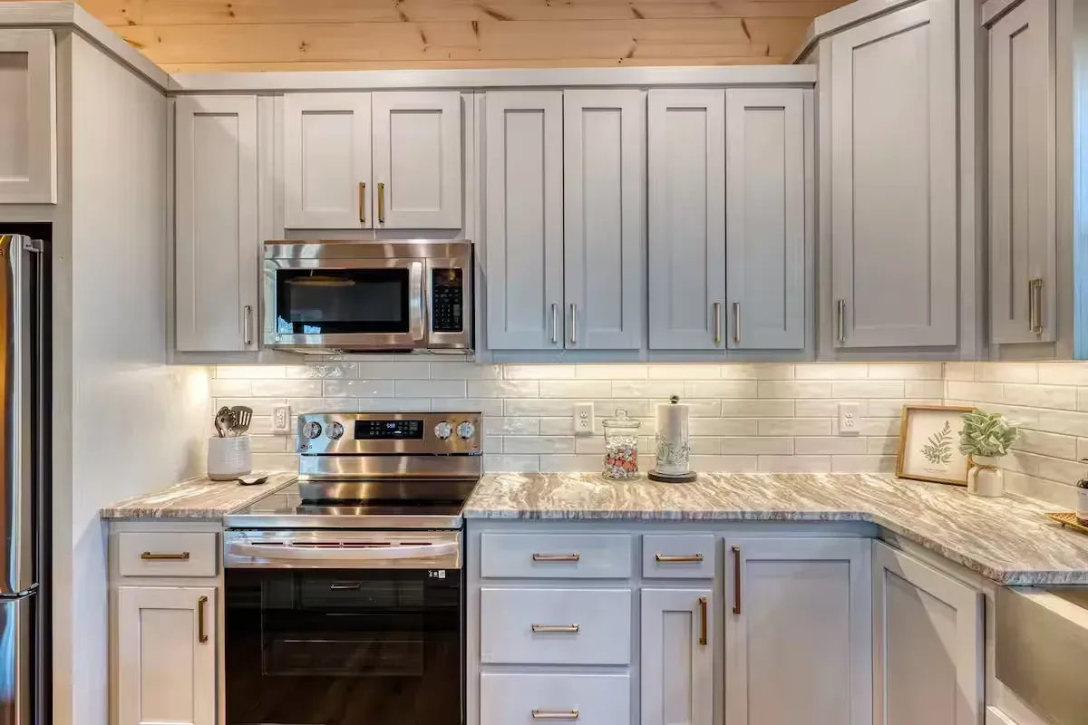 Modern kitchen with gray cabinets, stainless steel appliances, and light granite countertops