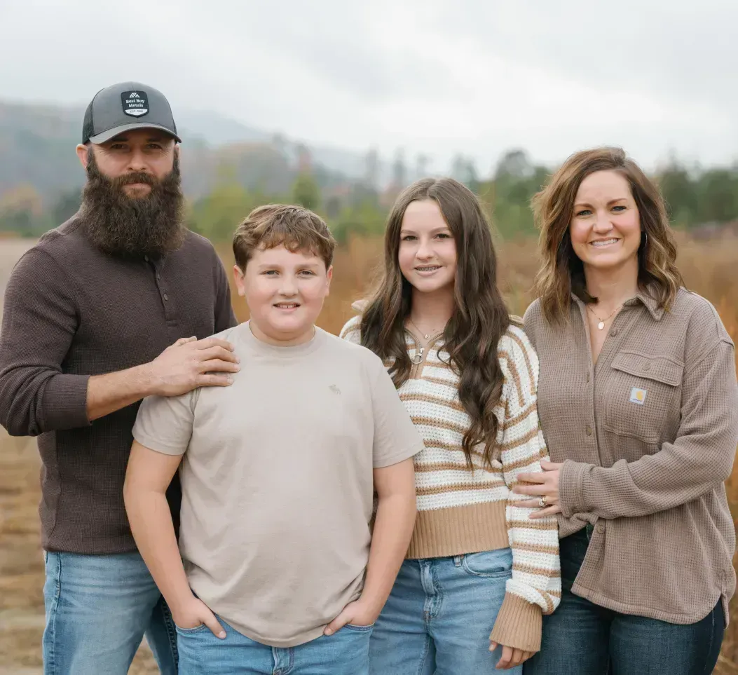 Family of four standing outdoors in a field, smiling at the camera with mountains in the background