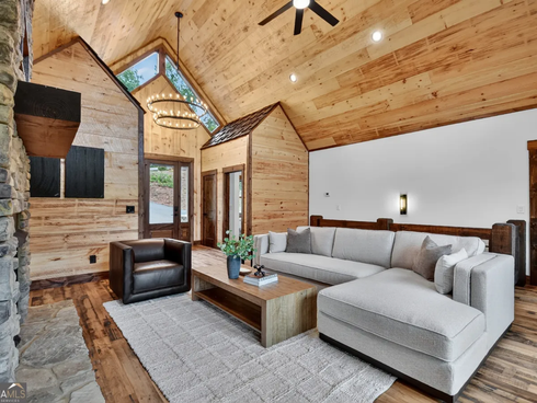 Cozy cabin living room with vaulted wood ceiling, gray sectional, armchair, and coffee table by large windows