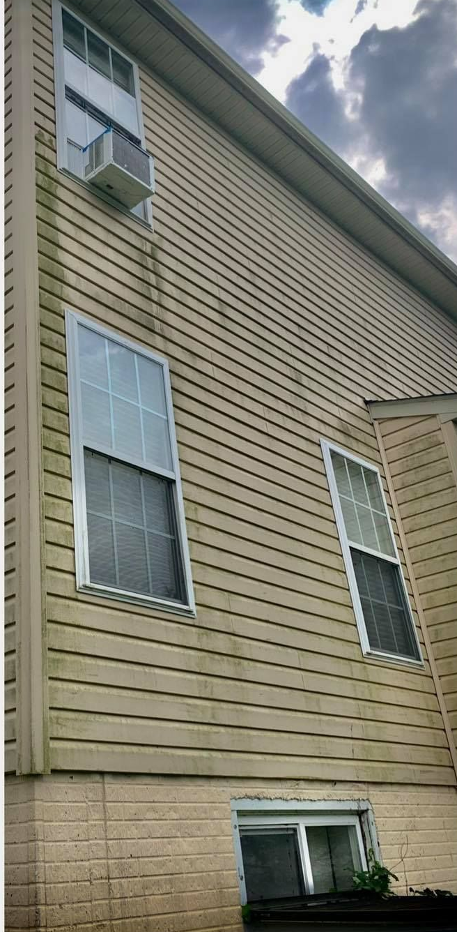 Exterior of a house with light tan siding, several windows, and an air conditioner unit. Cloudy sky overhead.