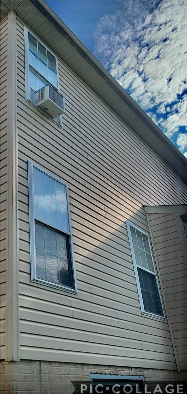 Side view of a beige house with multiple windows and an air conditioner. Blue sky with clouds.