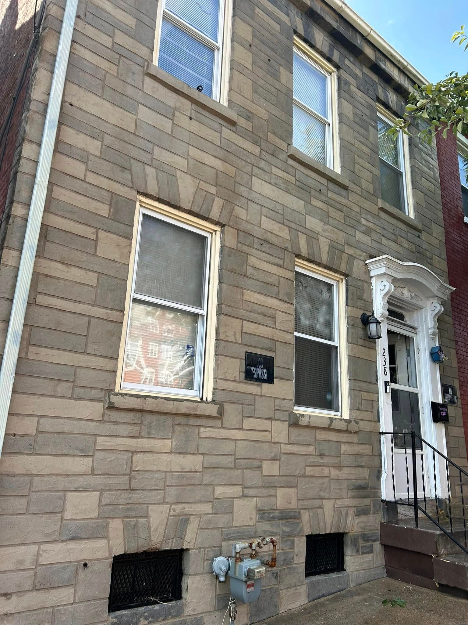 Two-story brick building with multiple windows. Light-colored stone facade and white door frame with steps.