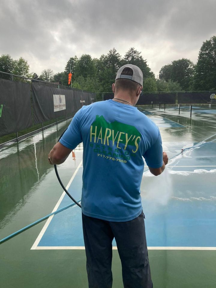 Man spraying water on a flooded tennis court, wearing a blue shirt with 