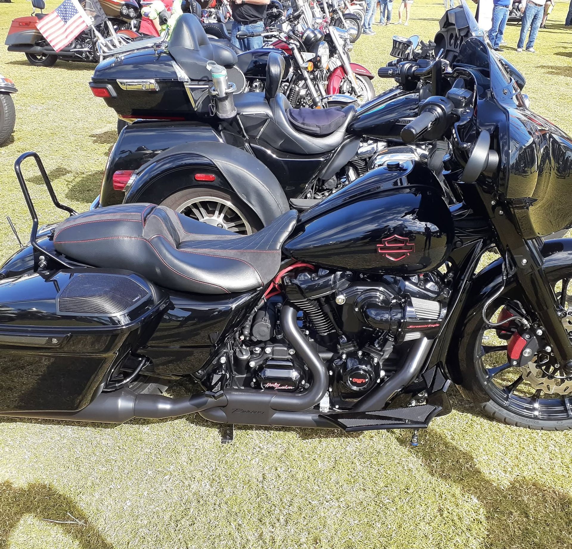 Black touring motorcycle parked on grass at an outdoor gathering, with other bikes and people in the background