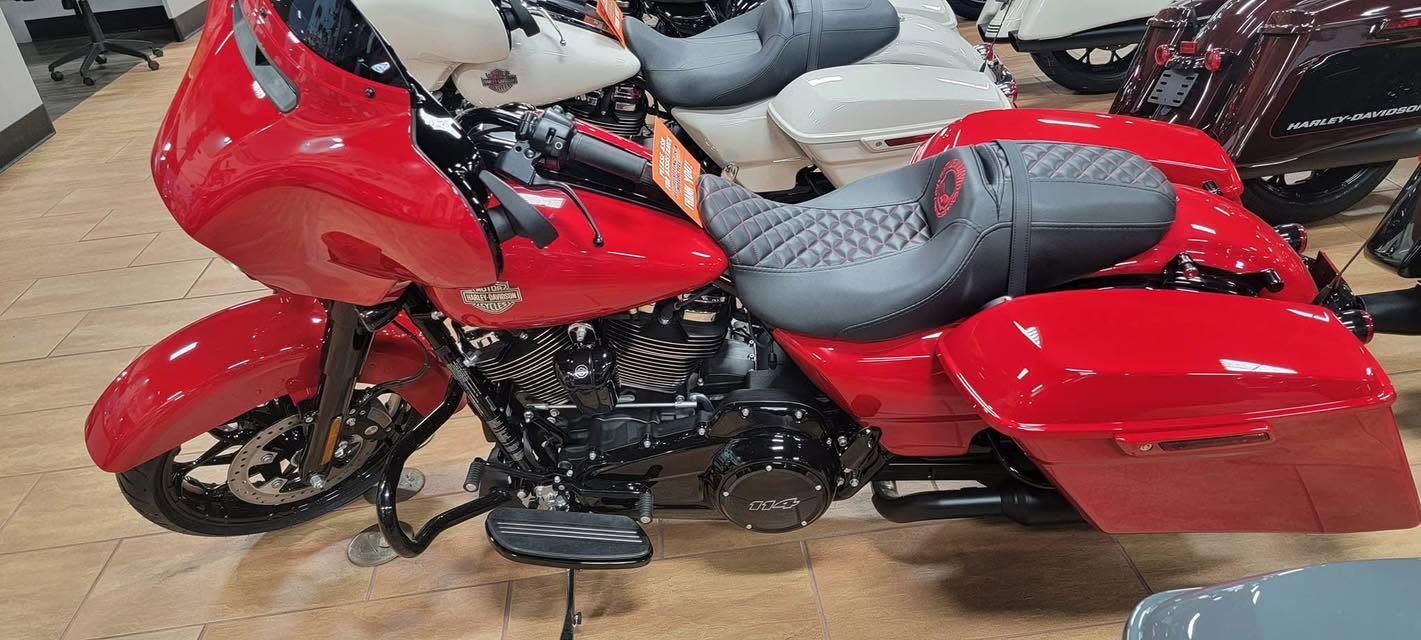 Red touring motorcycle with black seat parked indoors on a wooden floor.