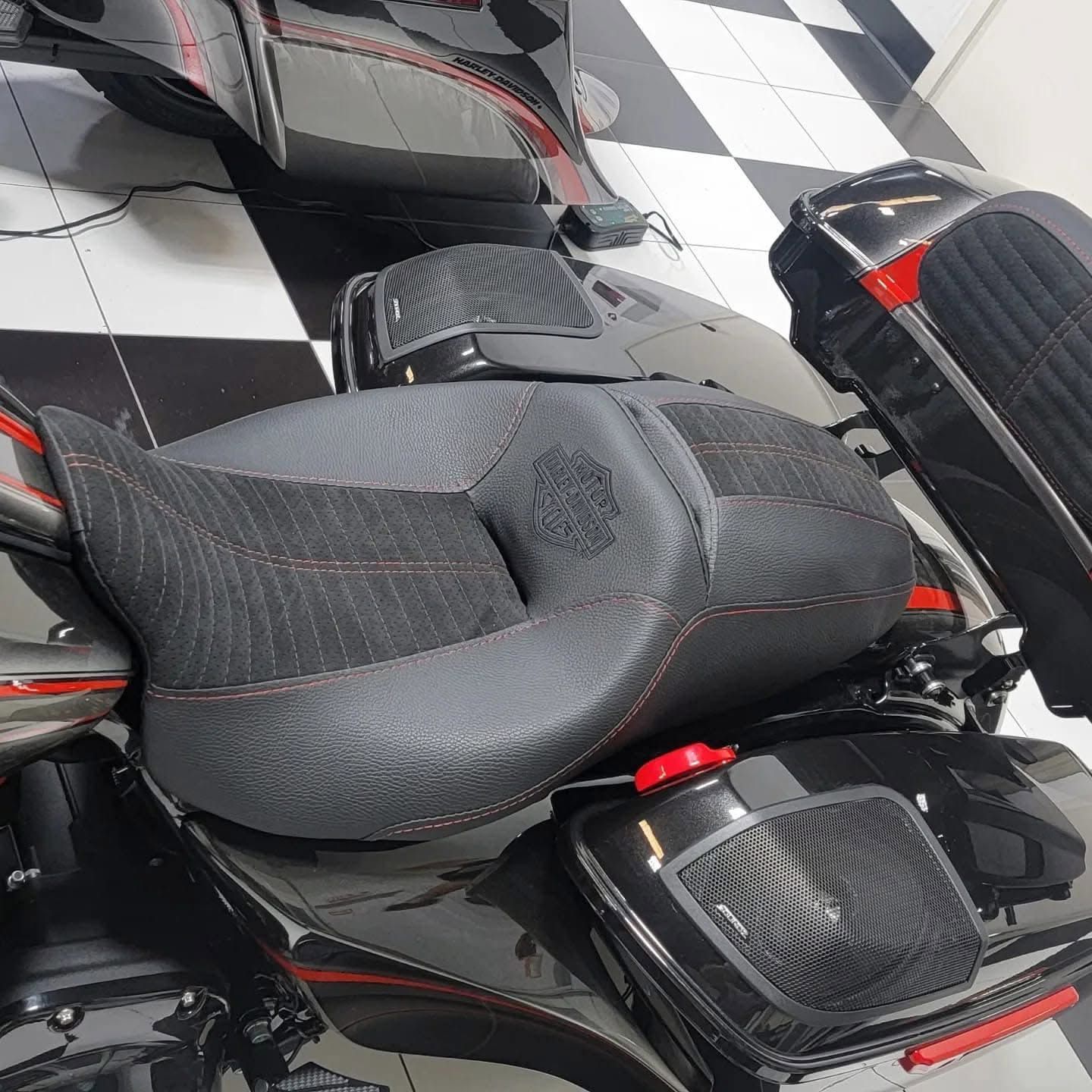Black motorcycle seat with a carbon-fiber texture on a black and red bike indoors on a checkered floor