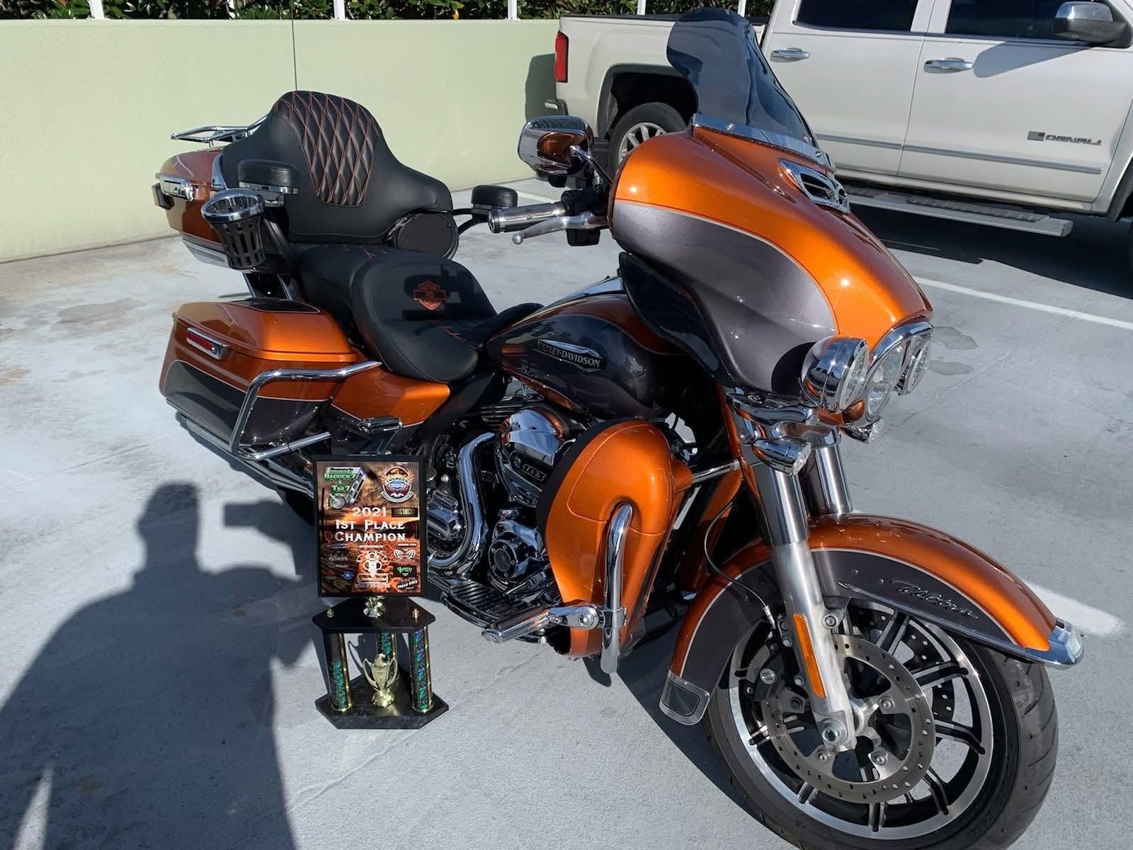 Orange touring motorcycle parked outdoors with black seat and accessories, in front of a white truck.