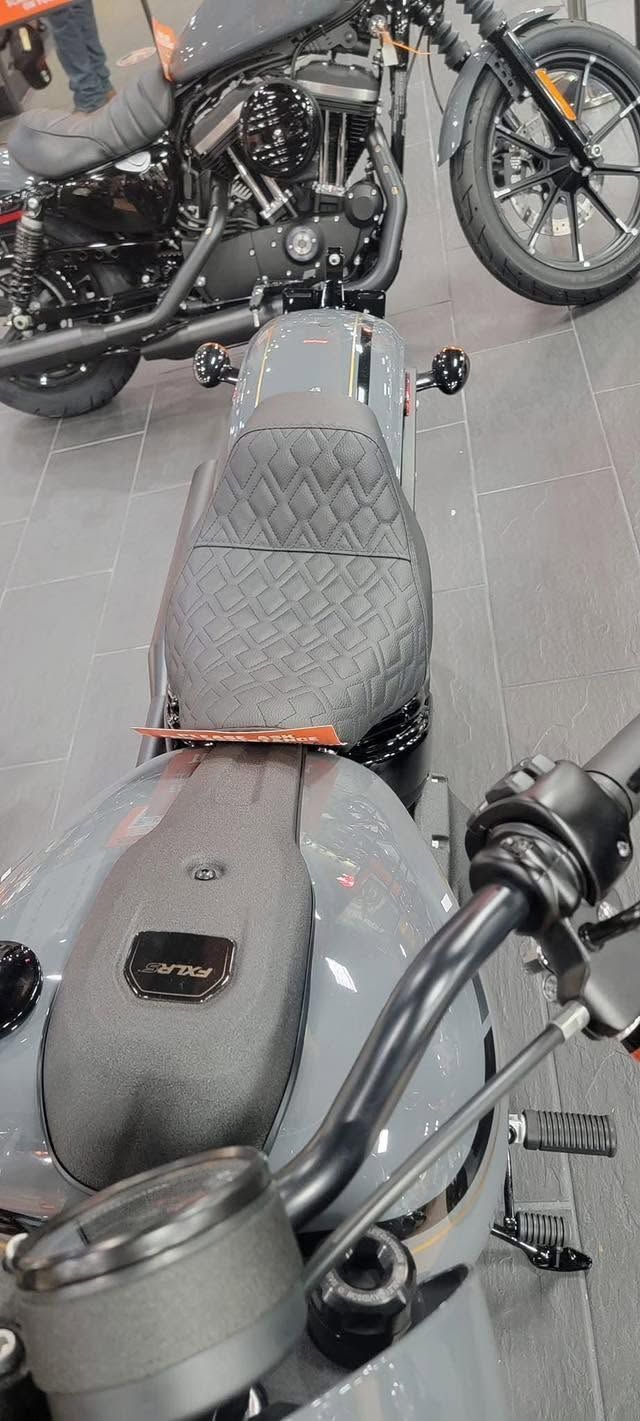 Gray motorcycle seat with a black fuel tank and handlebars in a garage, another bike in the background