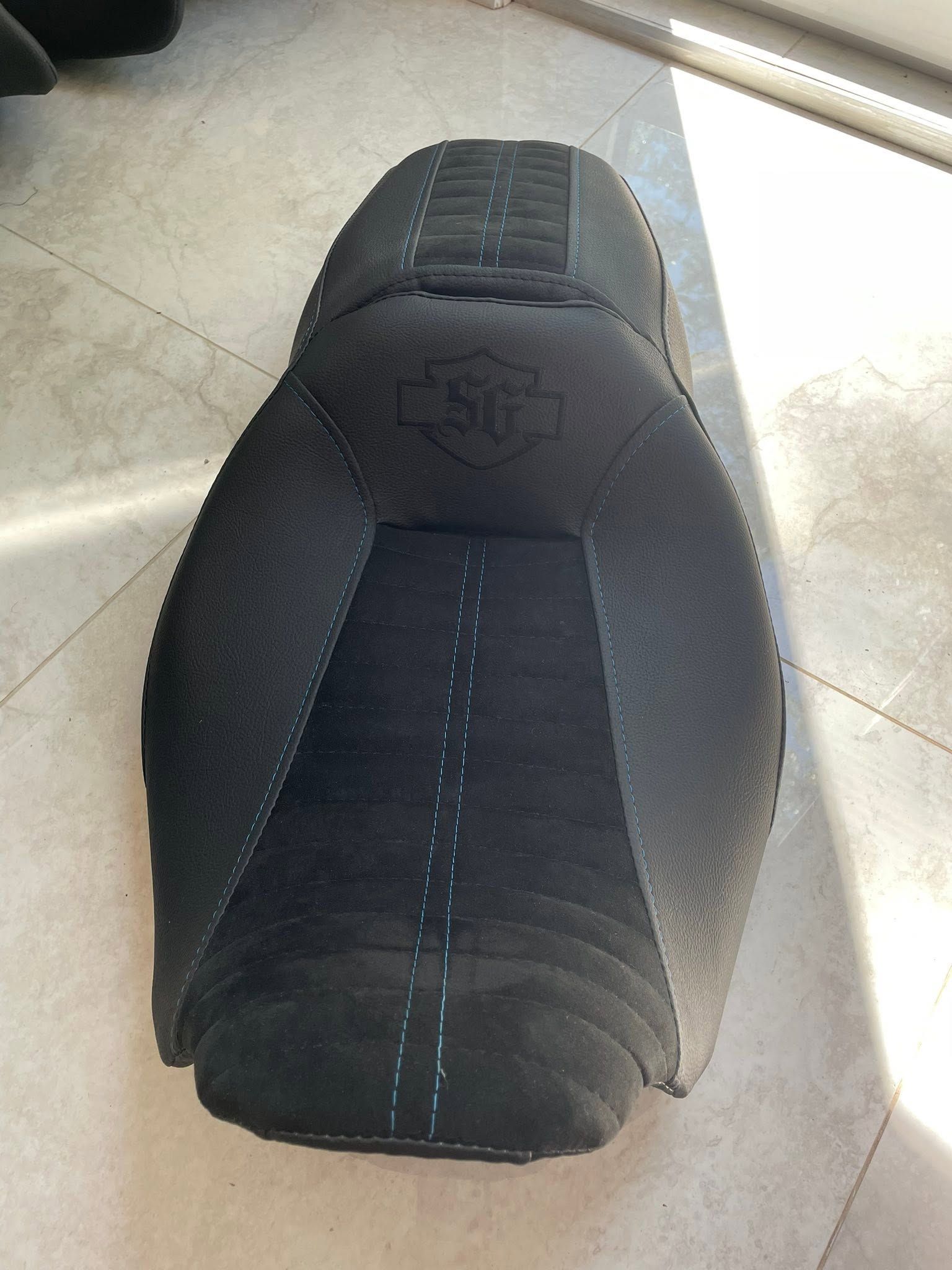 Black motorcycle seat viewed from above on a light tile floor