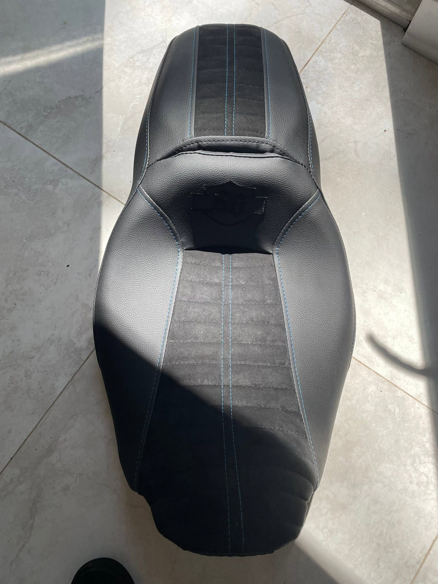 Black motorcycle/scooter seat with gray center stripe on a tiled floor, viewed from above