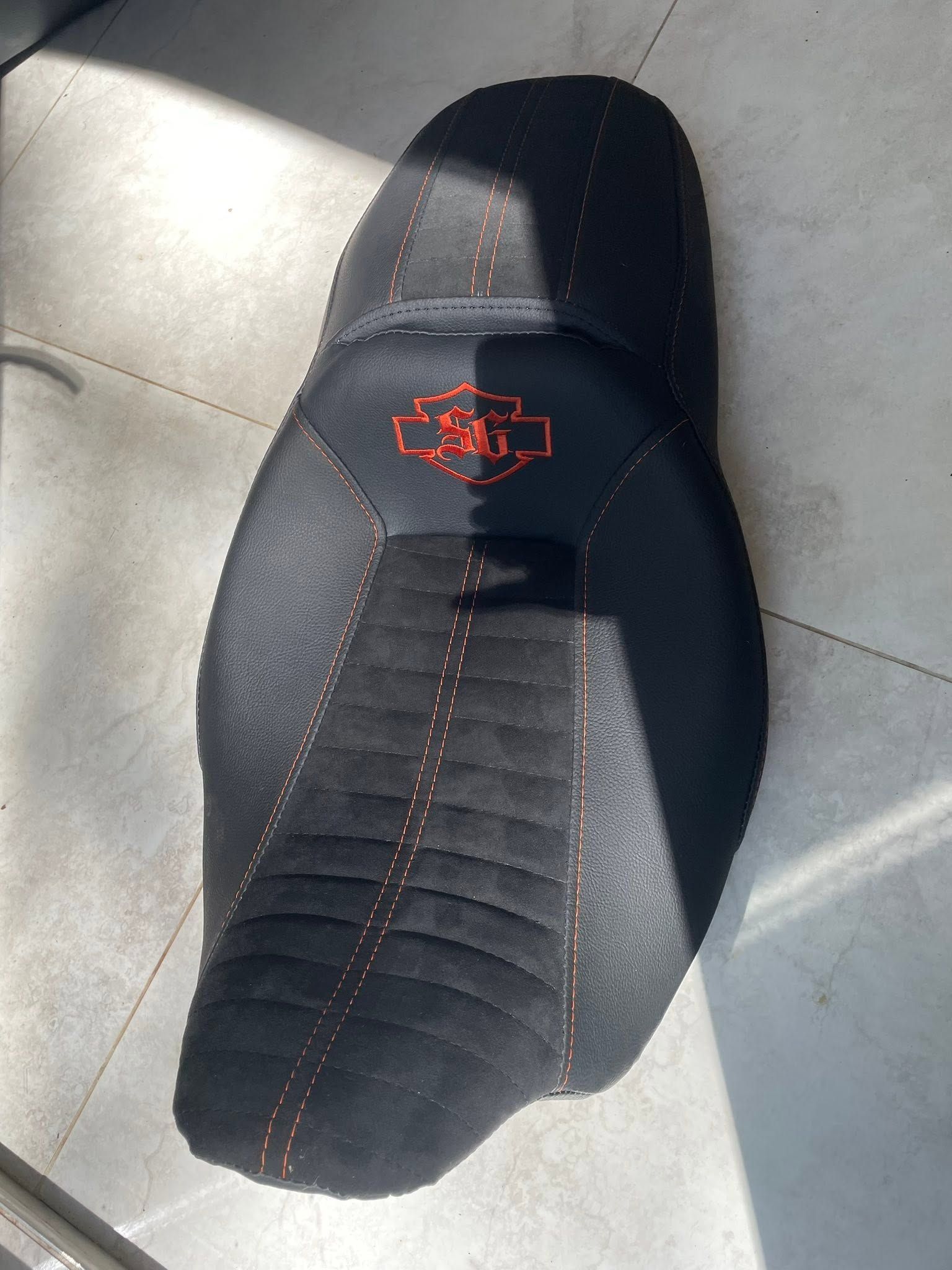 Black padded cycling saddle with red stitching, shown on a light tiled floor.