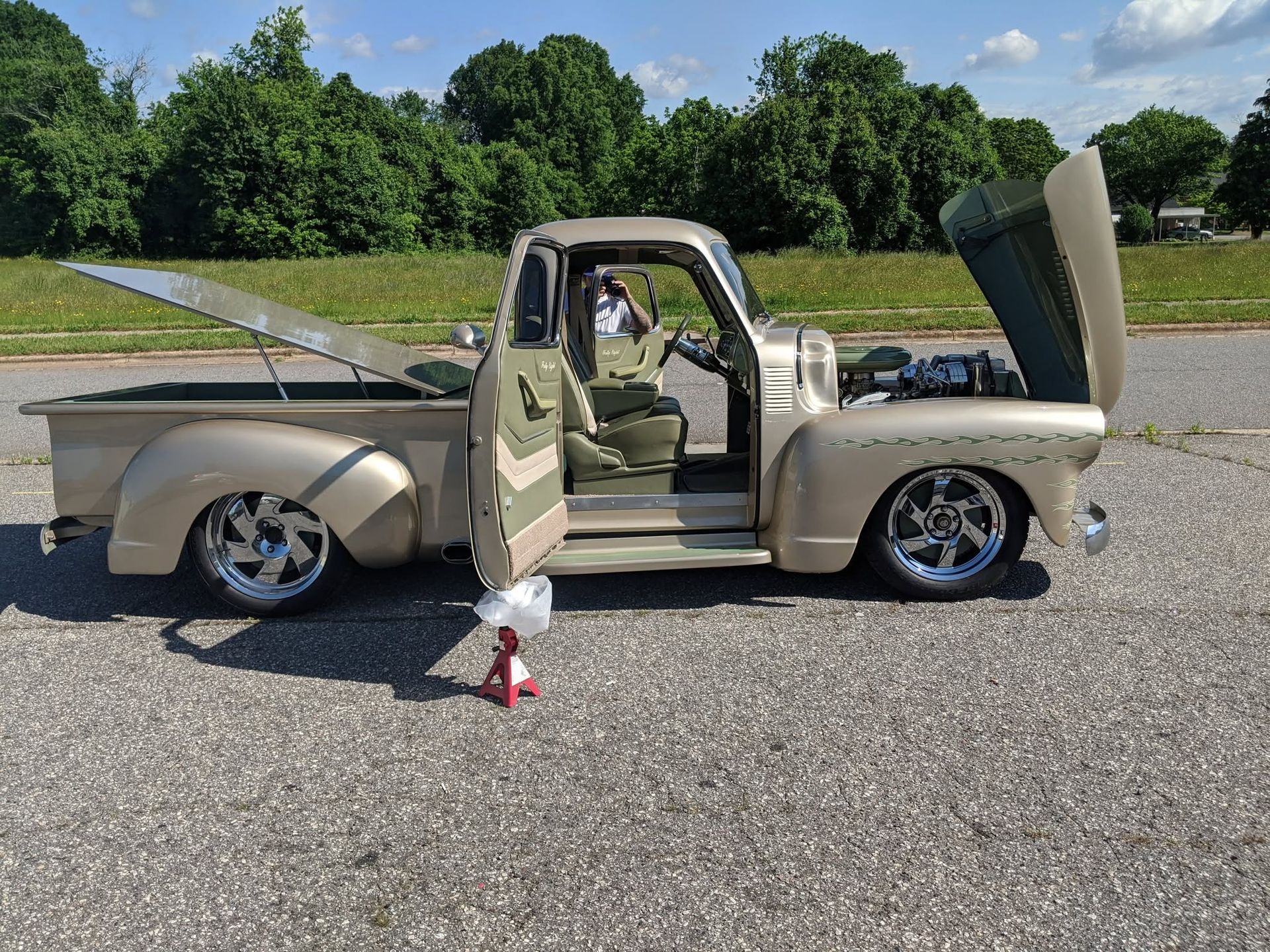 Beige custom pickup truck with hood open, parked on pavement with cones and trees in the background.