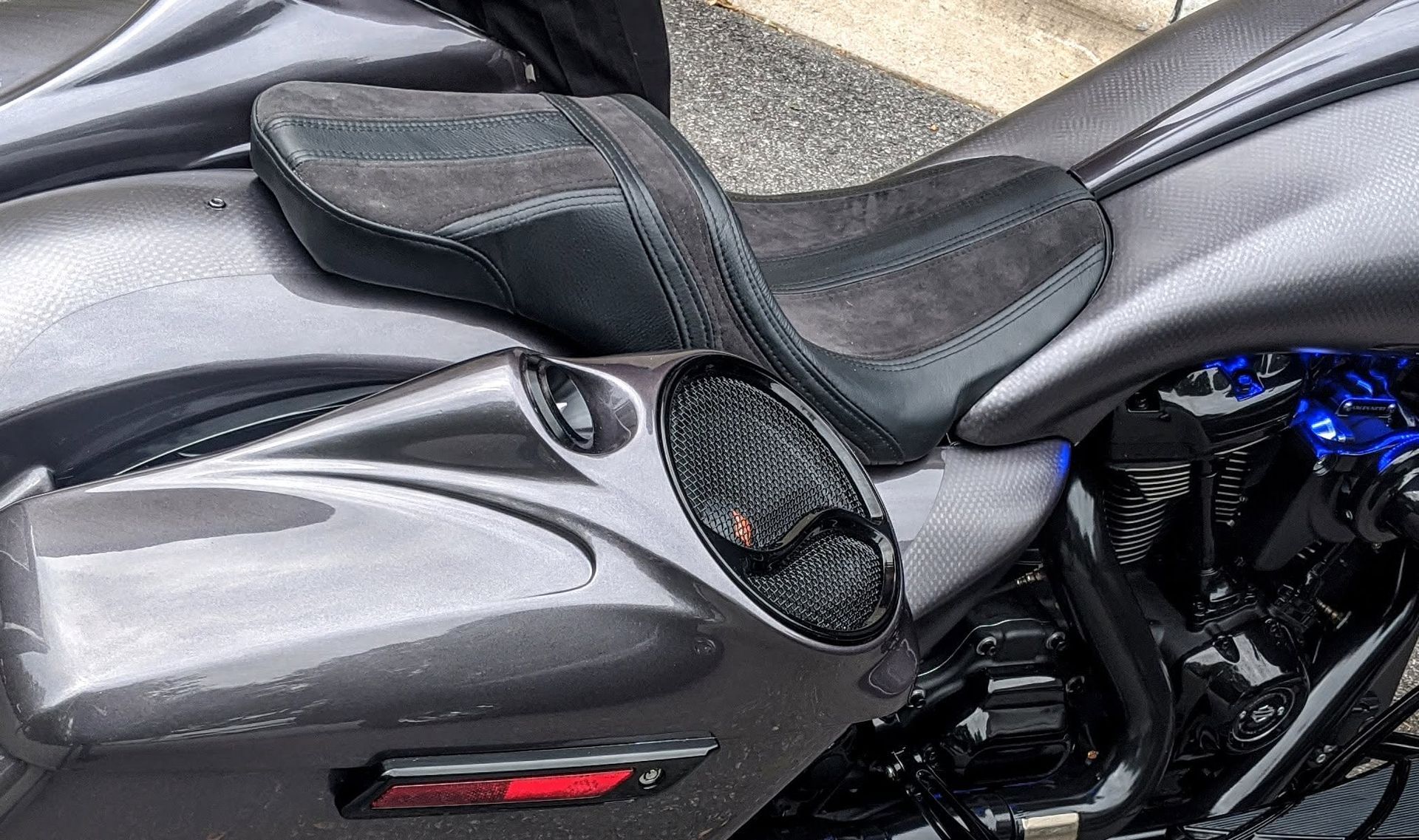 Black motorcycle seat and glossy side panel with a circular speaker-like detail and red reflector
