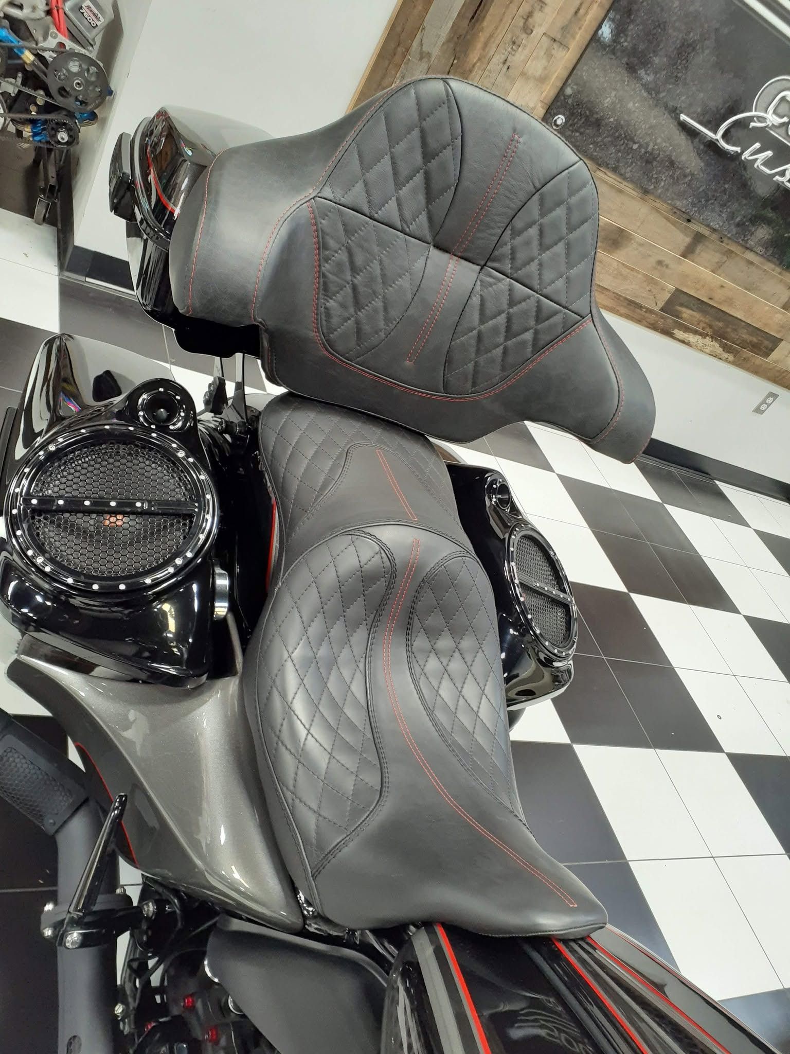 Gray motorcycle with stitched seat and rear backrest in a showroom, on a black-and-white checkered floor