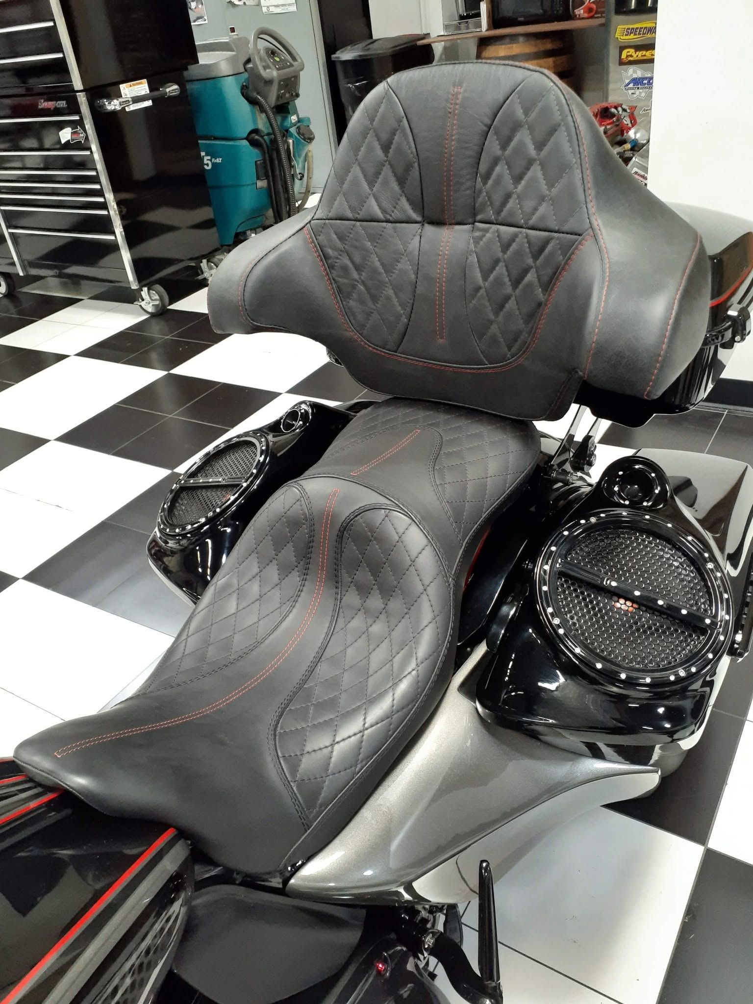 Custom black and gray motorcycle seat set on a black-and-white checkered floor in a workshop