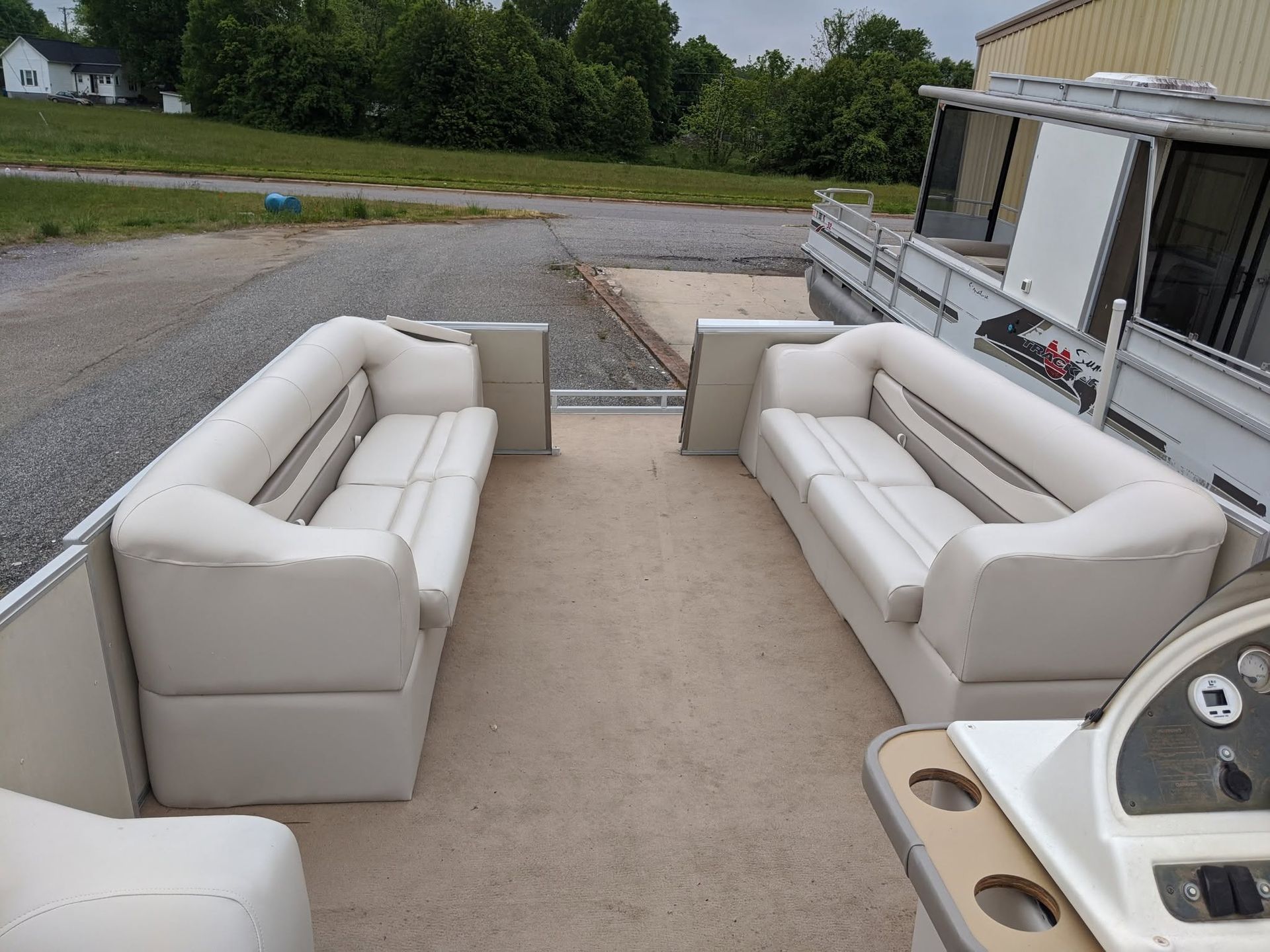 White patio sofas arranged on an outdoor deck beside a house, overlooking a gravel yard.
