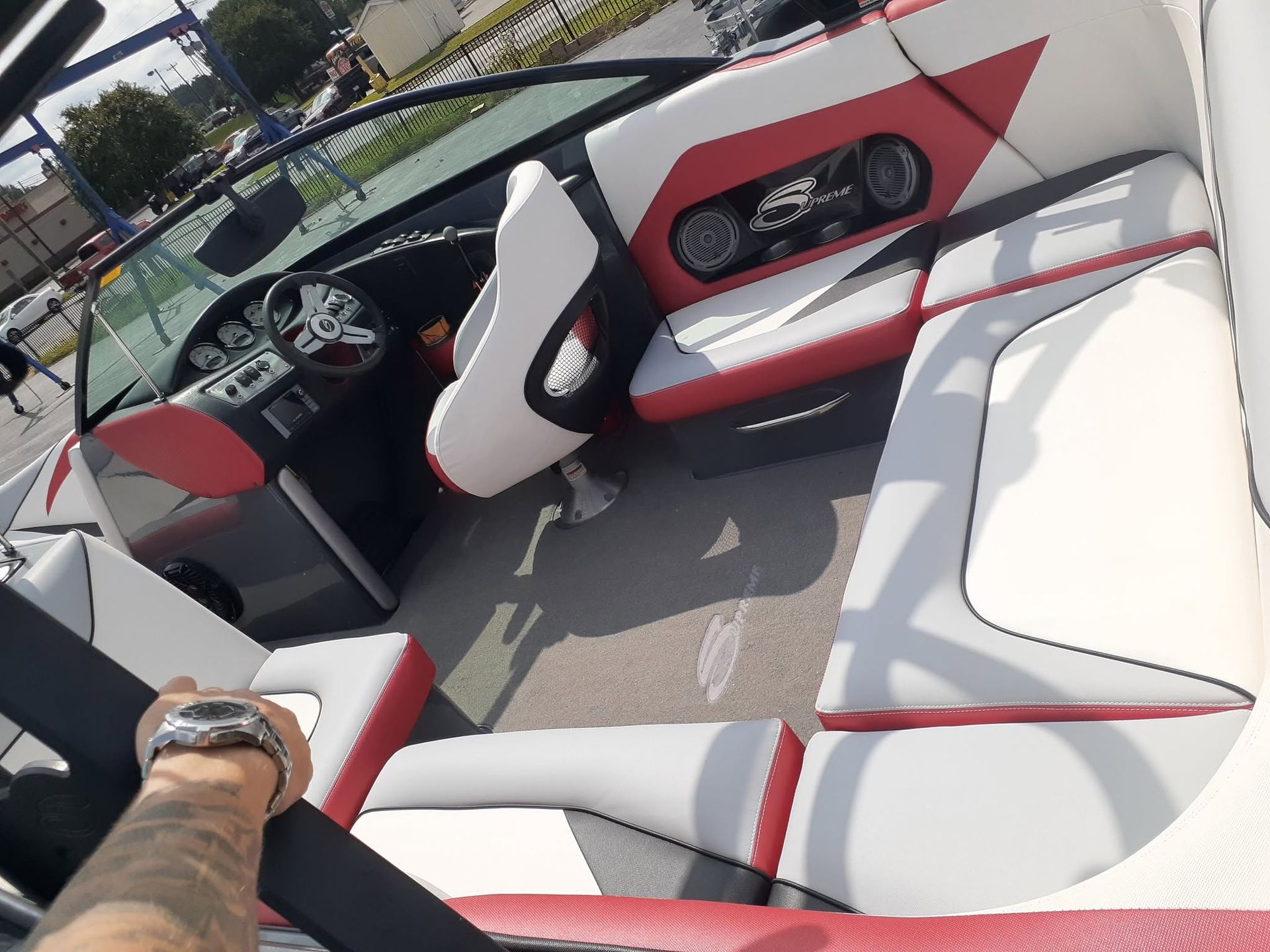 View from a boat cockpit with white and red seats, steering wheel, and dashboard on open water.