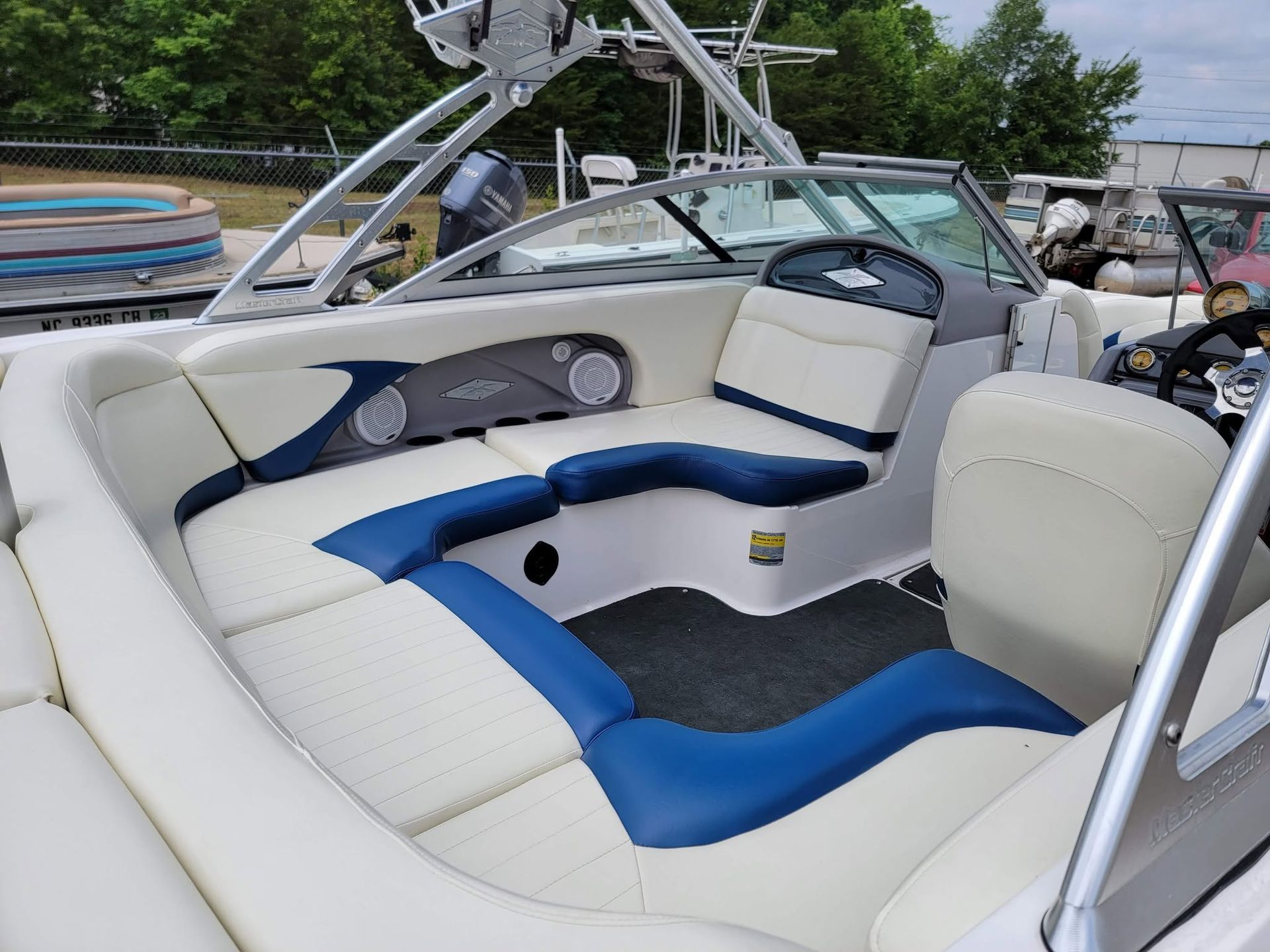 White and blue boat cockpit seating on a docked speedboat, with chrome rails and trees in the background
