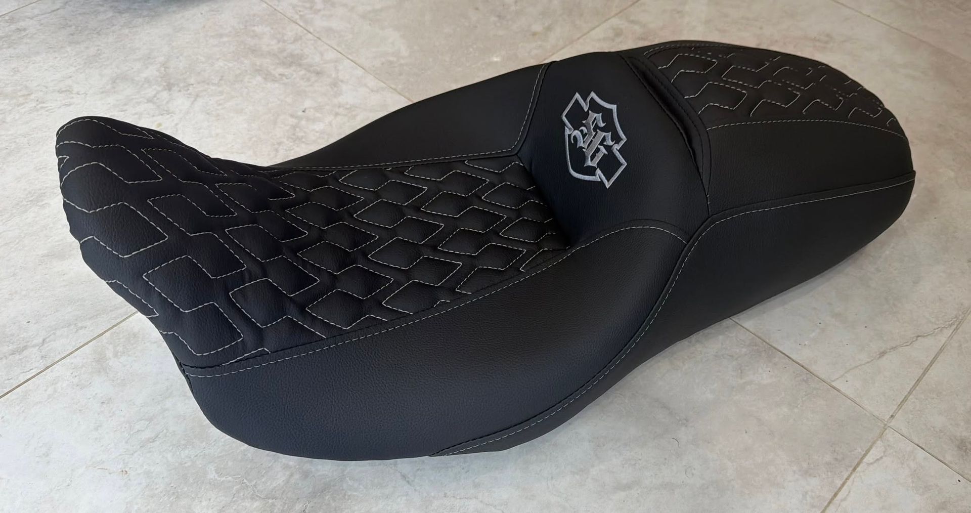 Black motorcycle seat with diamond-stitched top and Harley-Davidson logo on a tiled floor