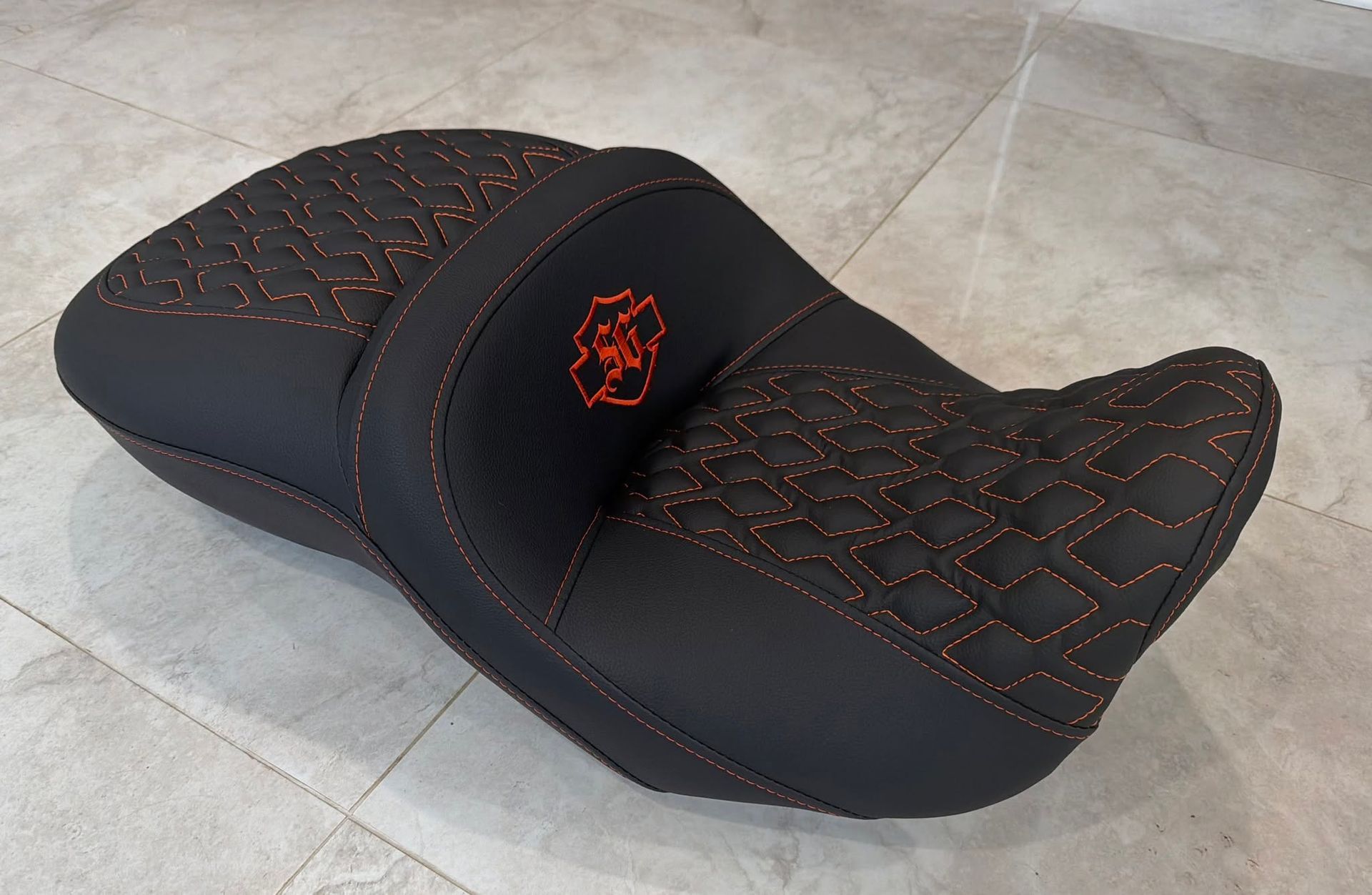 Black quilted motorcycle seat with red stitching on a tiled floor