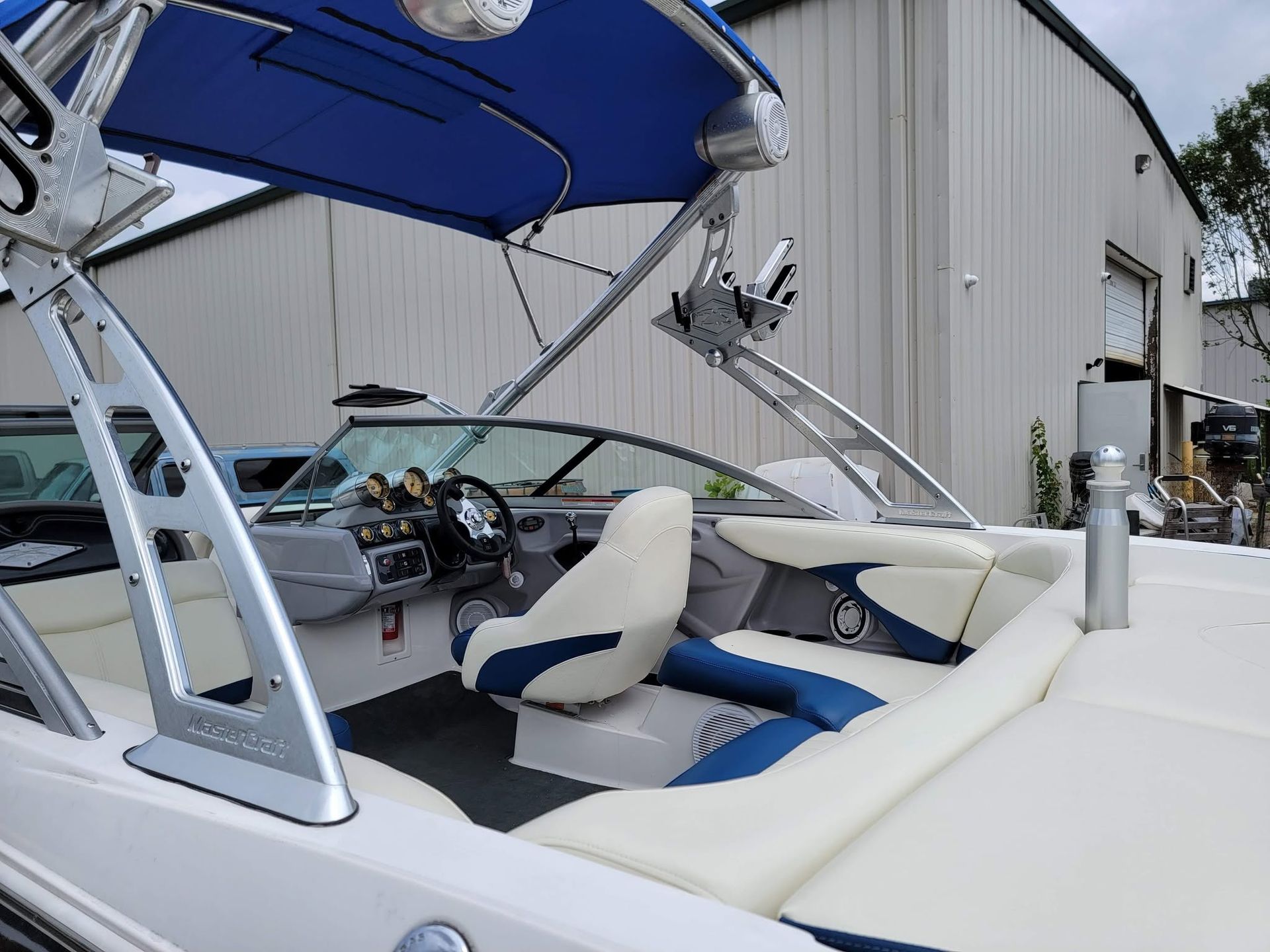 Boat cockpit with white and blue seating under a raised canopy beside a building