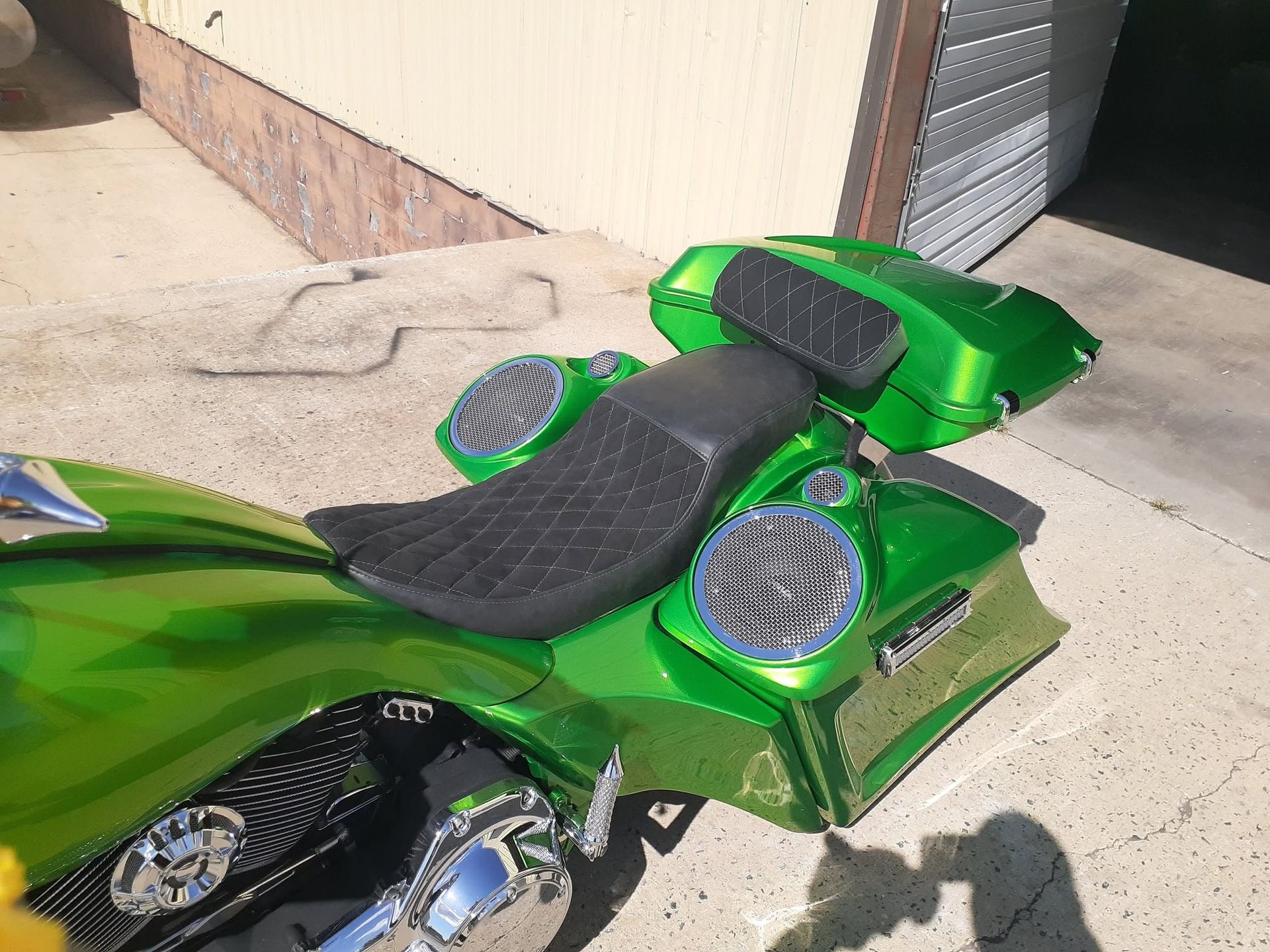 Green custom motorcycle parked by a building, showing chrome details and black seat in bright sunlight