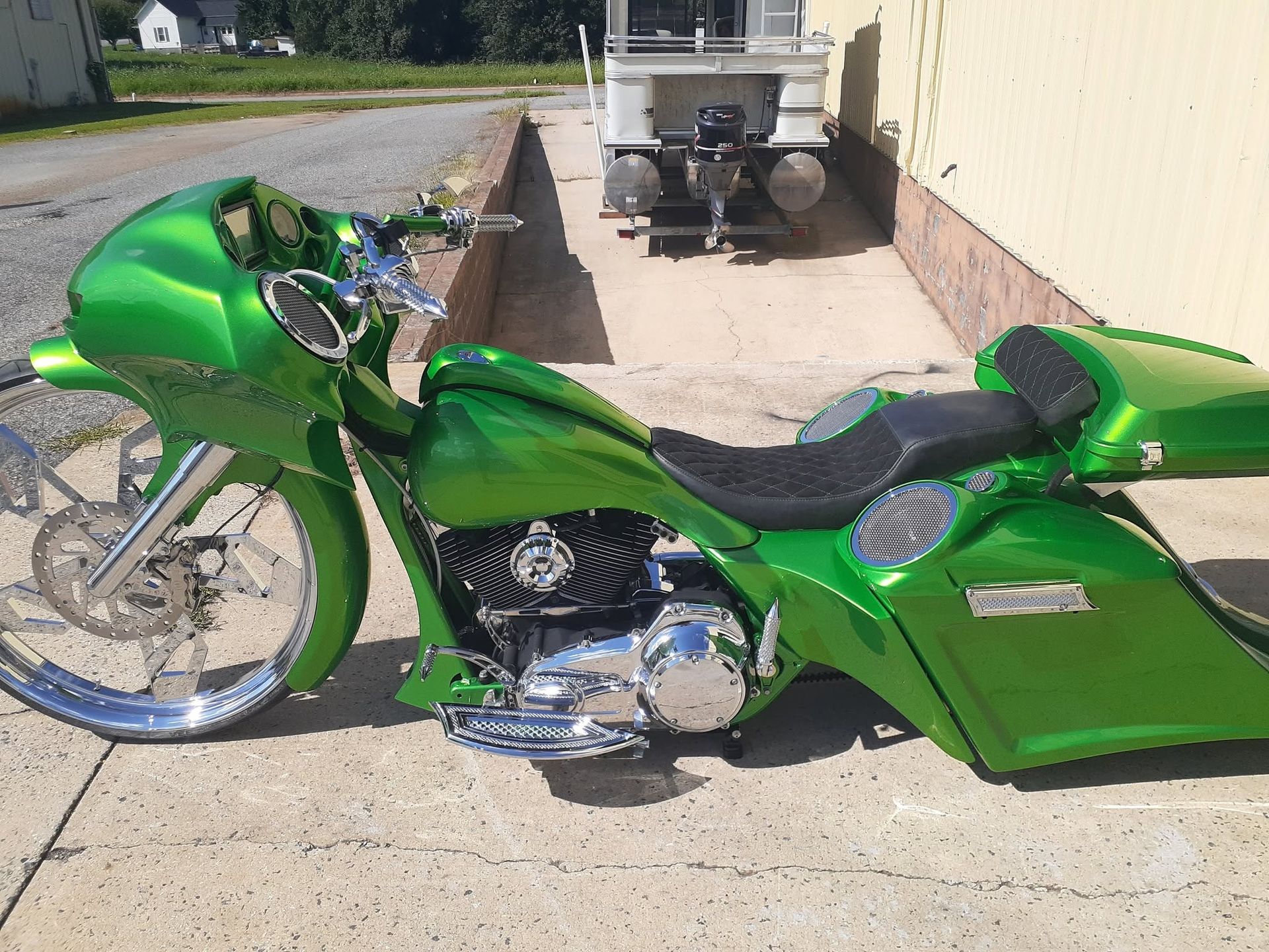 Green custom motorcycle parked on a sidewalk beside a building, with chrome wheels and bodywork.