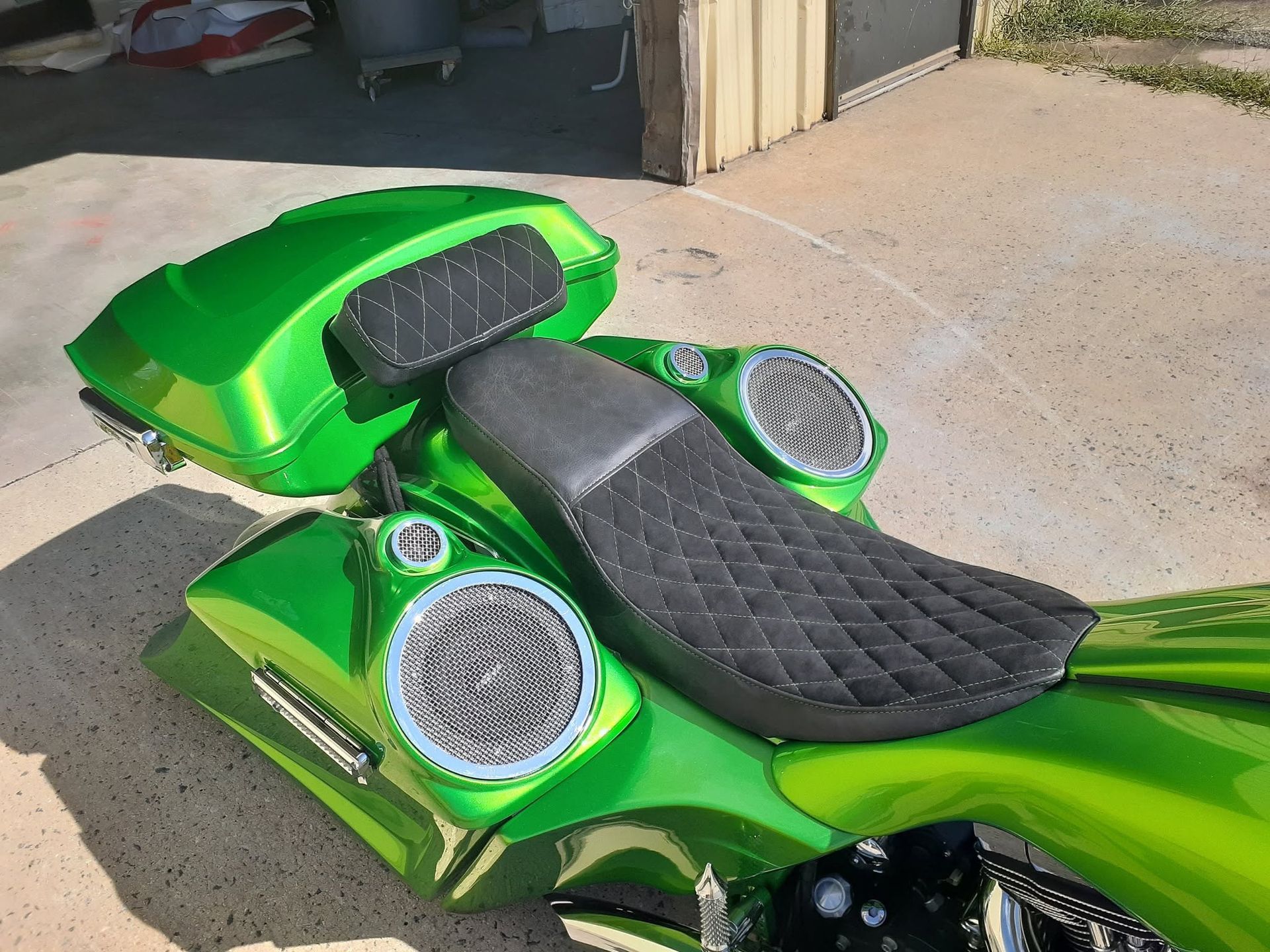 Bright green custom motorcycle seat with black quilted upholstery and silver speakers in a garage.