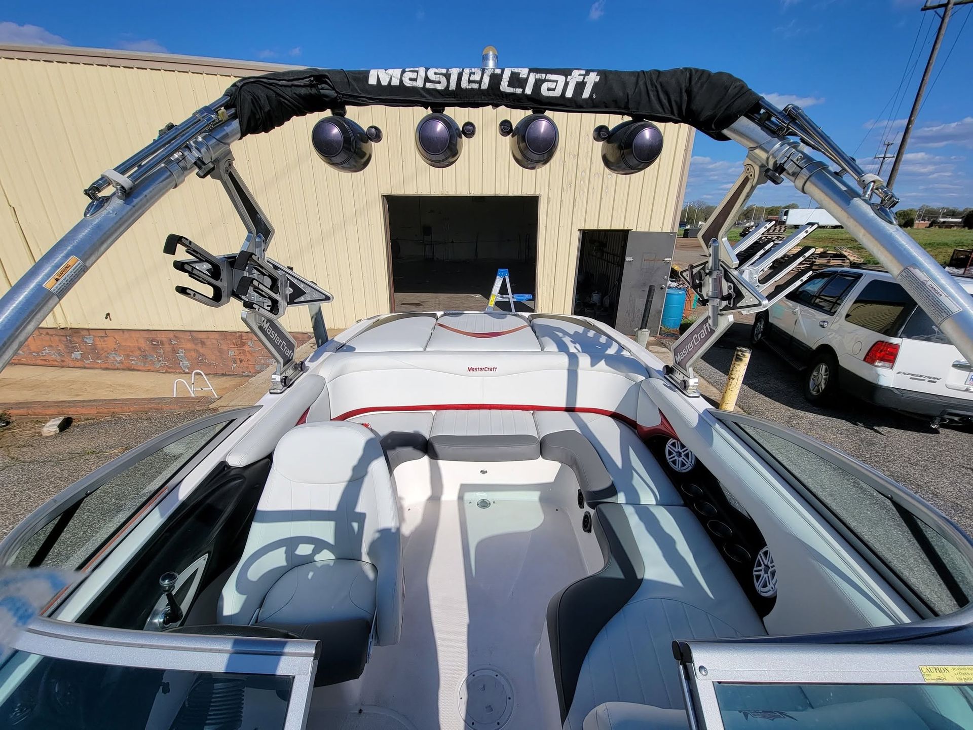 View from a boat showing a metal wakeboard tower in front of a MastCraft shop and parked vehicles