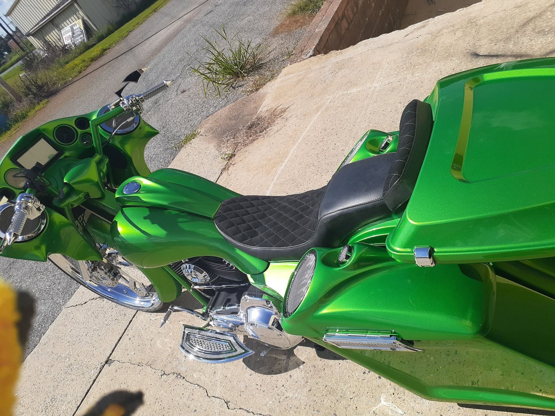Green motorcycle with black seat parked on a paved surface beside a curb.