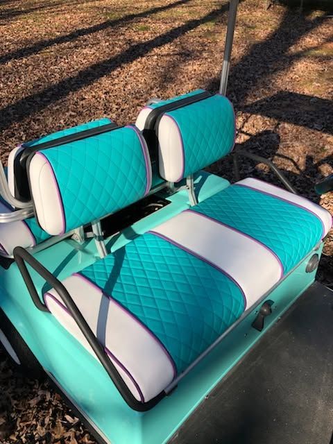 Turquoise and white padded bench seat with headrests on a metal frame outdoors on pavement and leaves