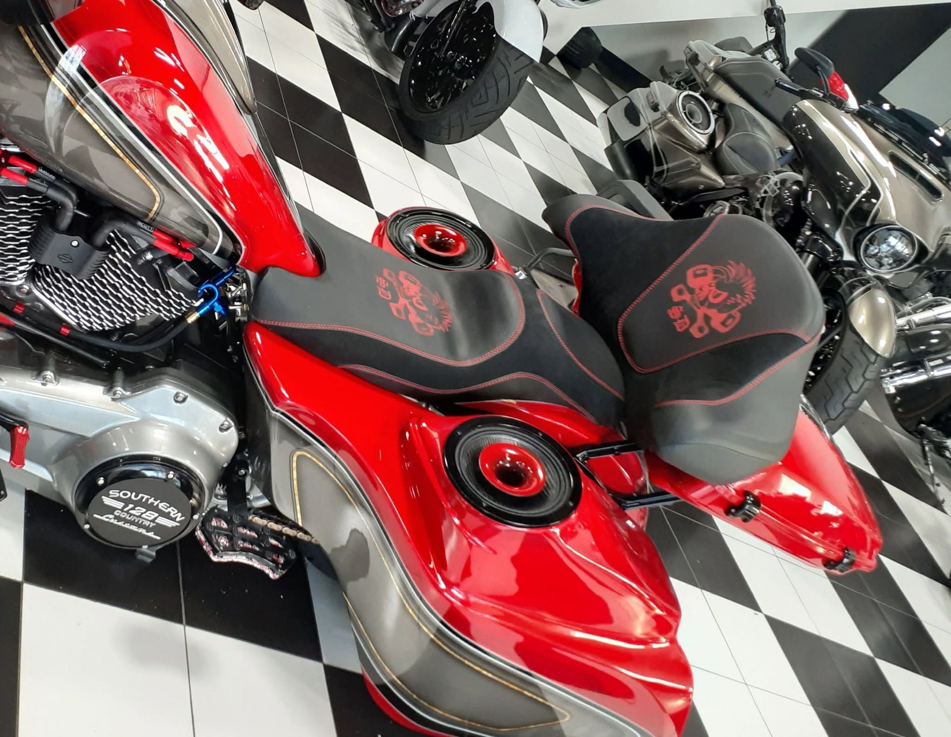 Red custom motorcycle with black seat on a black-and-white checkered floor in a showroom