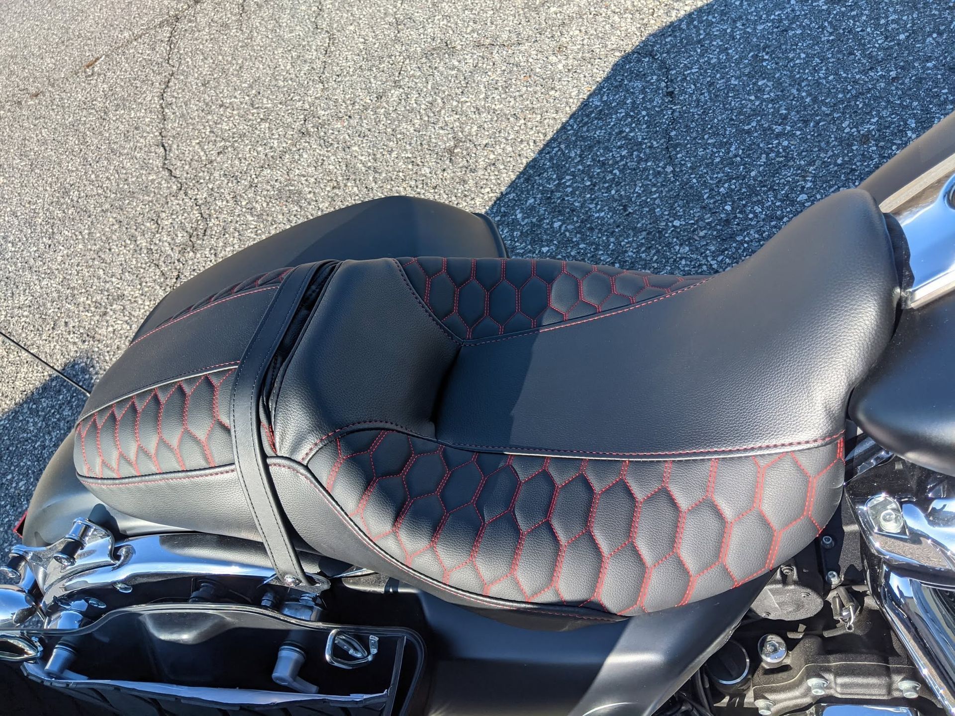 Black motorcycle seat with red stitching and a stitched diamond pattern, shown in close-up.