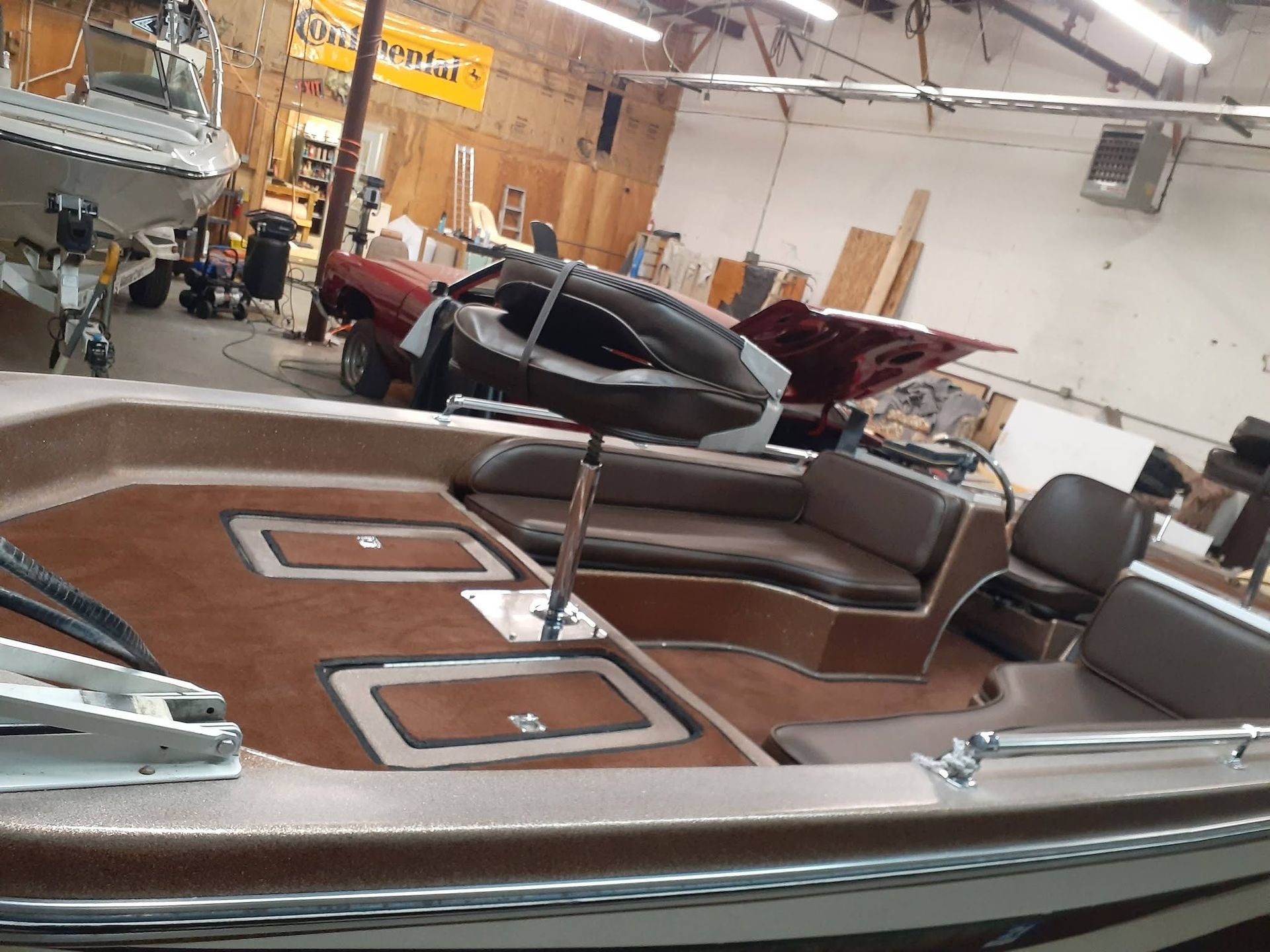 Brown and chrome vintage speedboat in a workshop, with open cockpit seating and a central steering wheel.