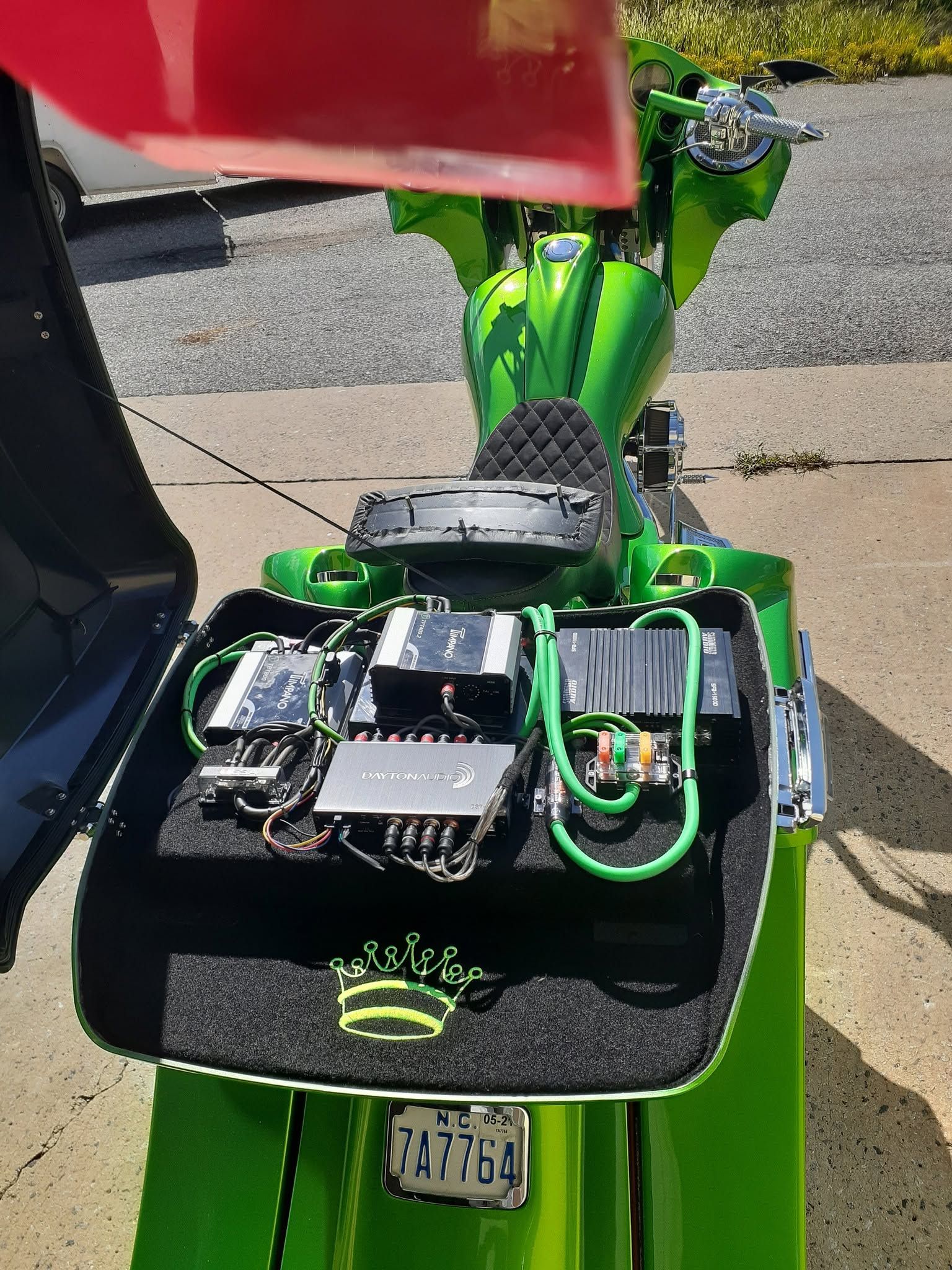 Green mobility scooter with exposed electronics parked outdoors on a sidewalk.
