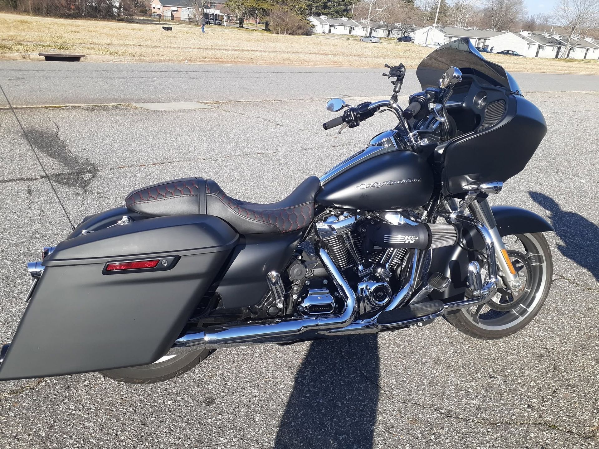 Black touring motorcycle with saddlebags parked on gravel in a sunny outdoor lot.