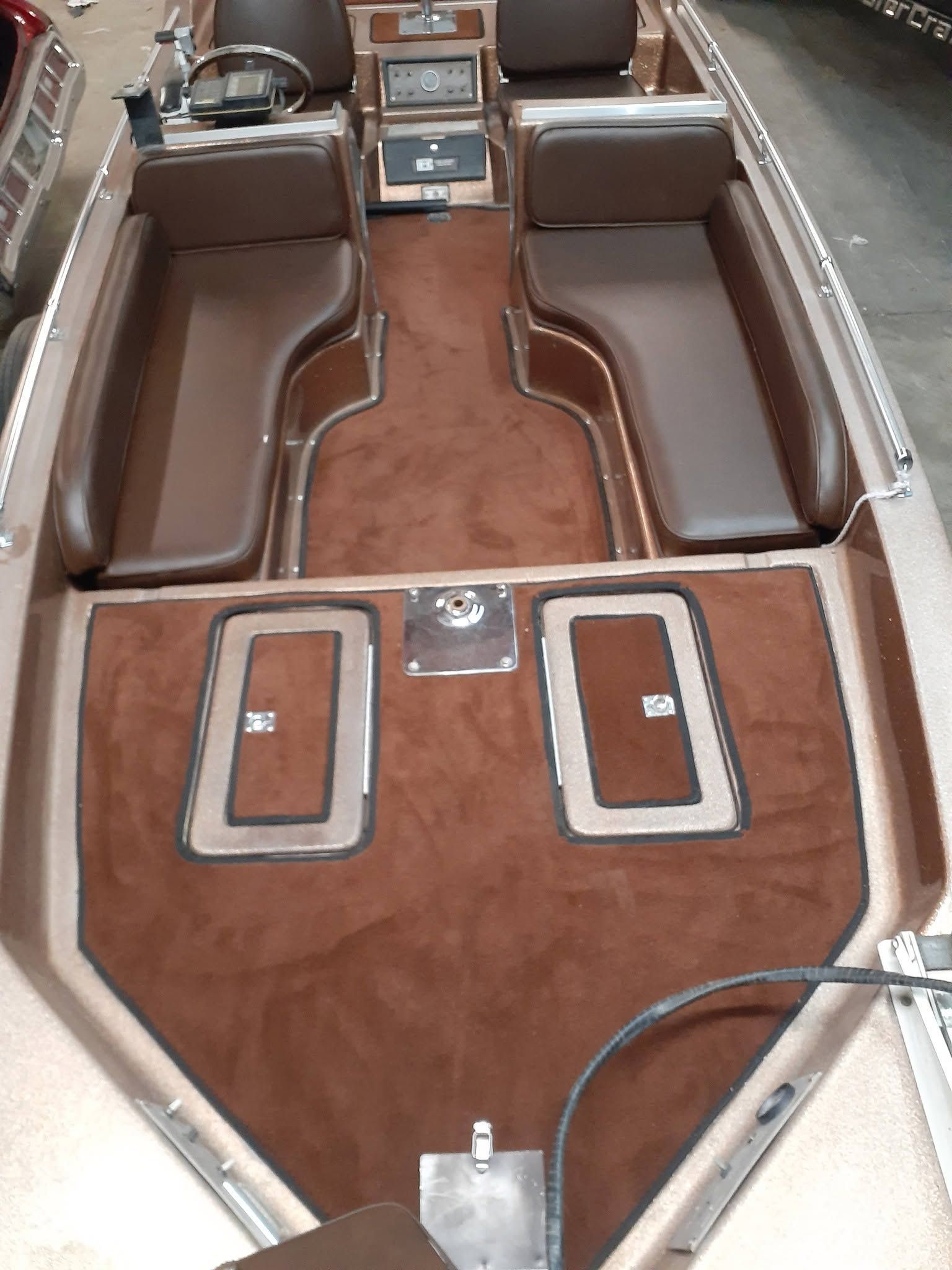Brown-and-tan vintage boat interior with cushioned benches and central controls, viewed from the bow