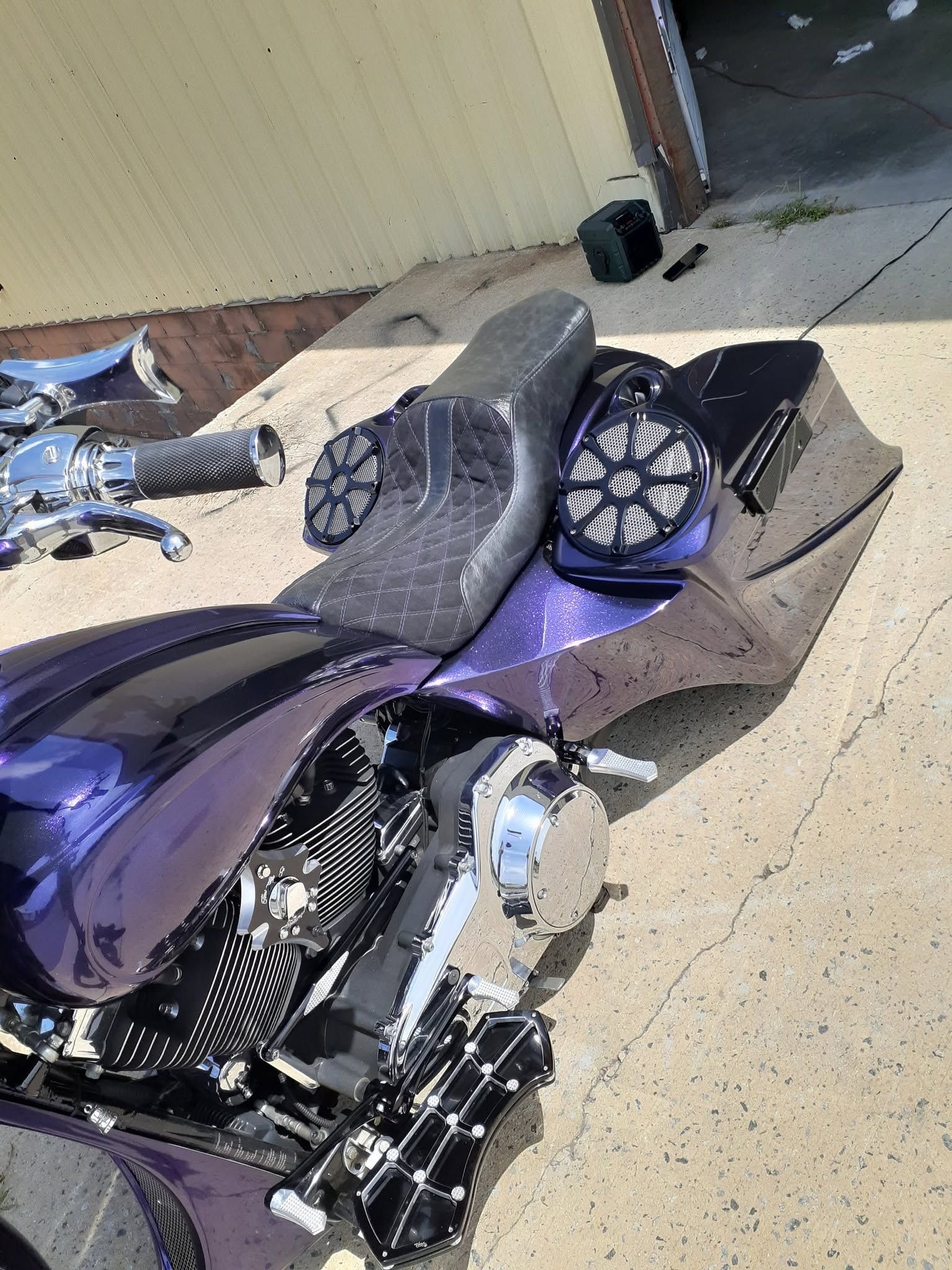 Purple motorcycle parked beside a beige wall with a black saddlebag and chrome engine parts