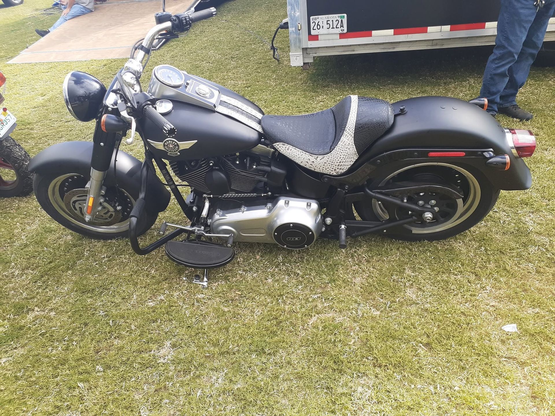 Black cruiser motorcycle parked on grass beside a trailer, with a person standing nearby