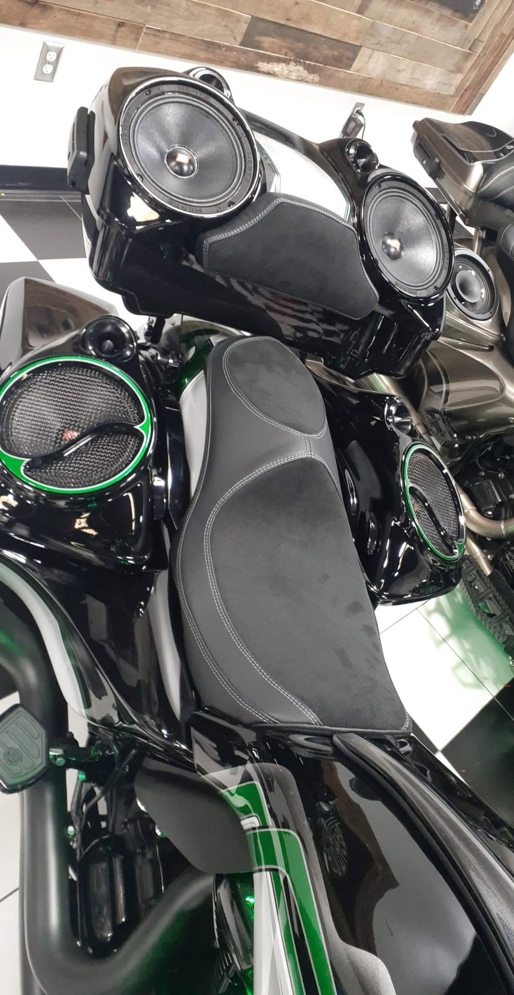 Black motorcycle dashboard and handlebars, with a leather seat and green accent lights in a garage.