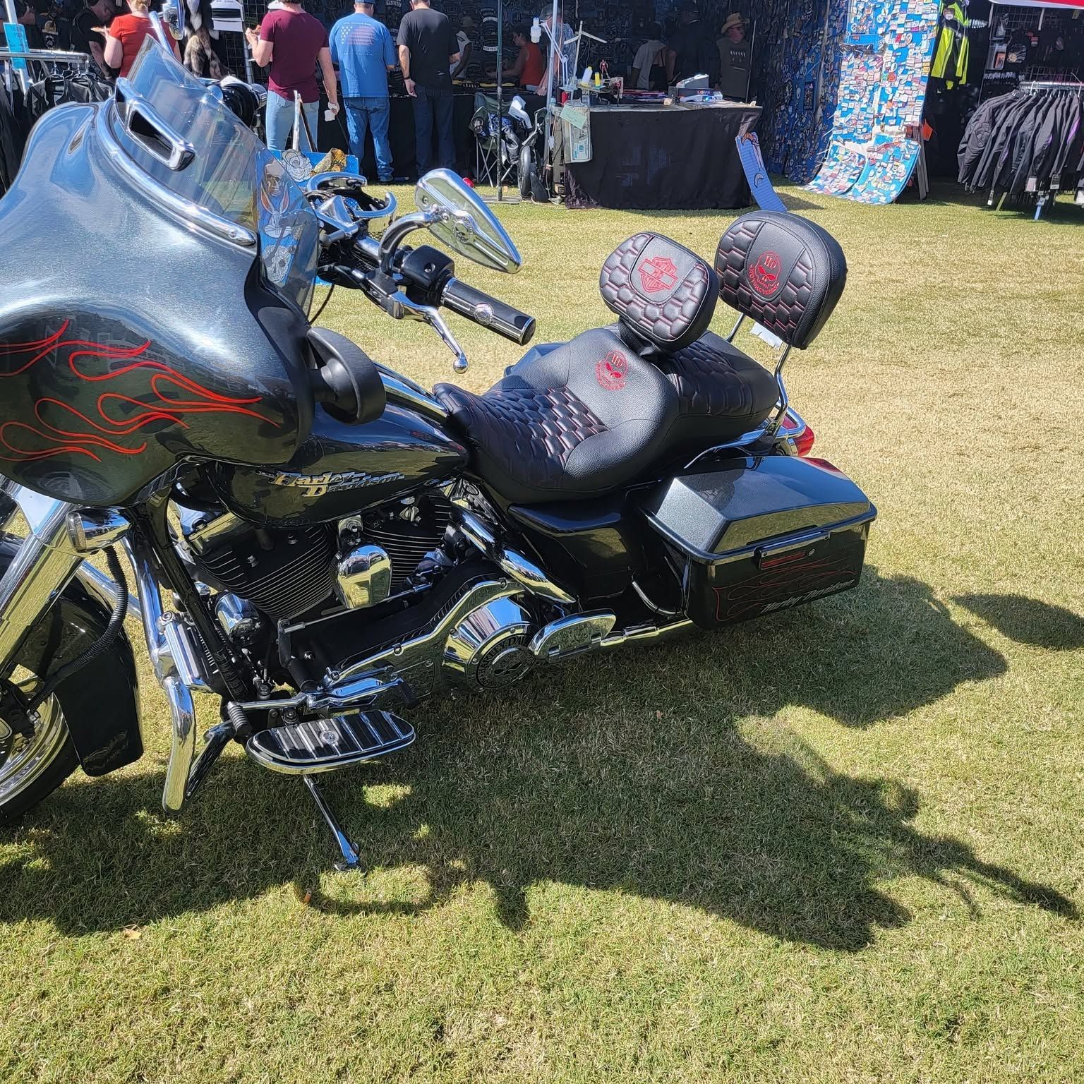 Black touring motorcycle parked on grass at an outdoor event, with red-accented seats and speakers.