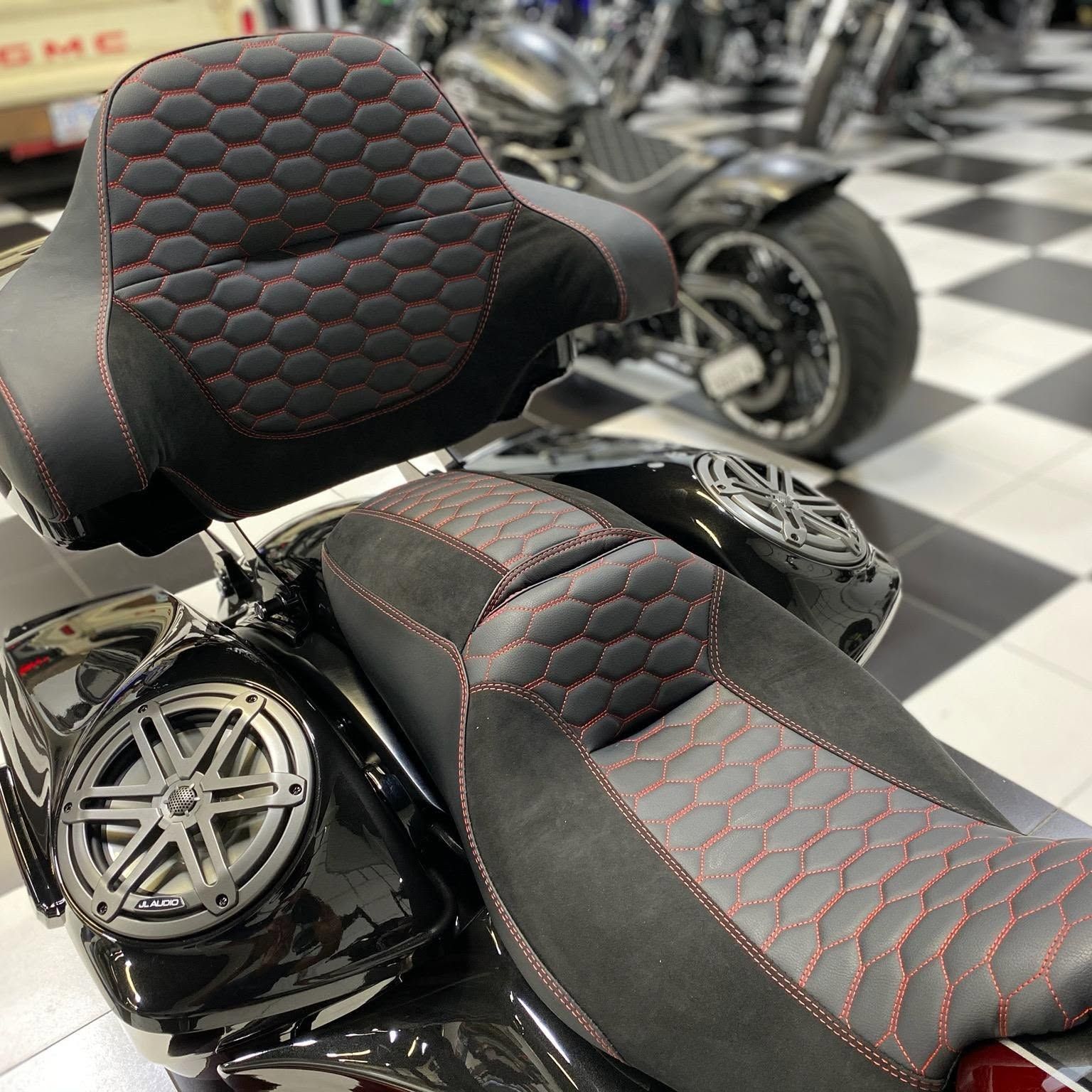 Black custom motorcycle seat with red stitching in a showroom, with chrome wheels in the background